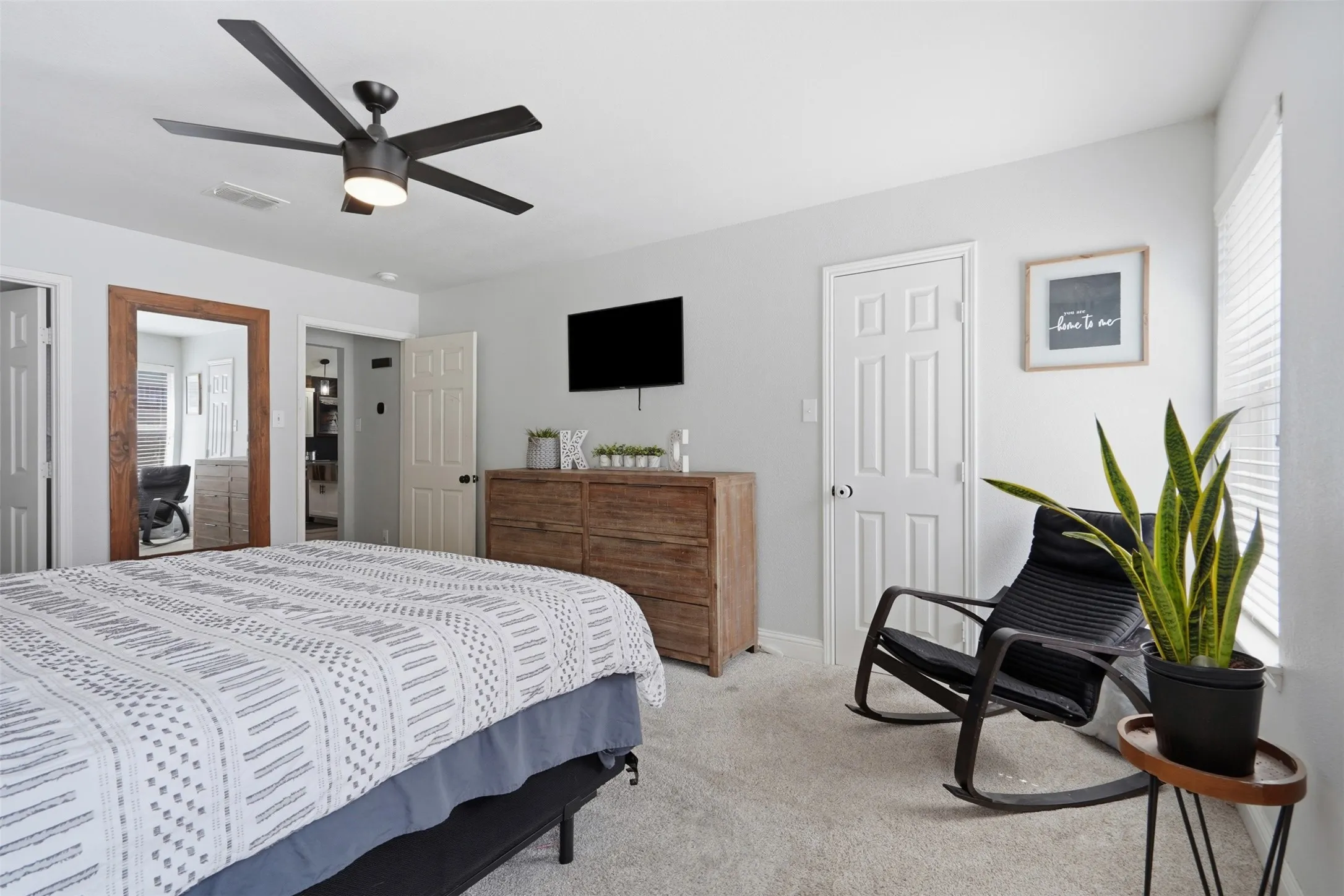 Light-filled room featuring a ceiling fan with integrated lighting, wood-finish flooring, a full-length mirror, and white paneled doors