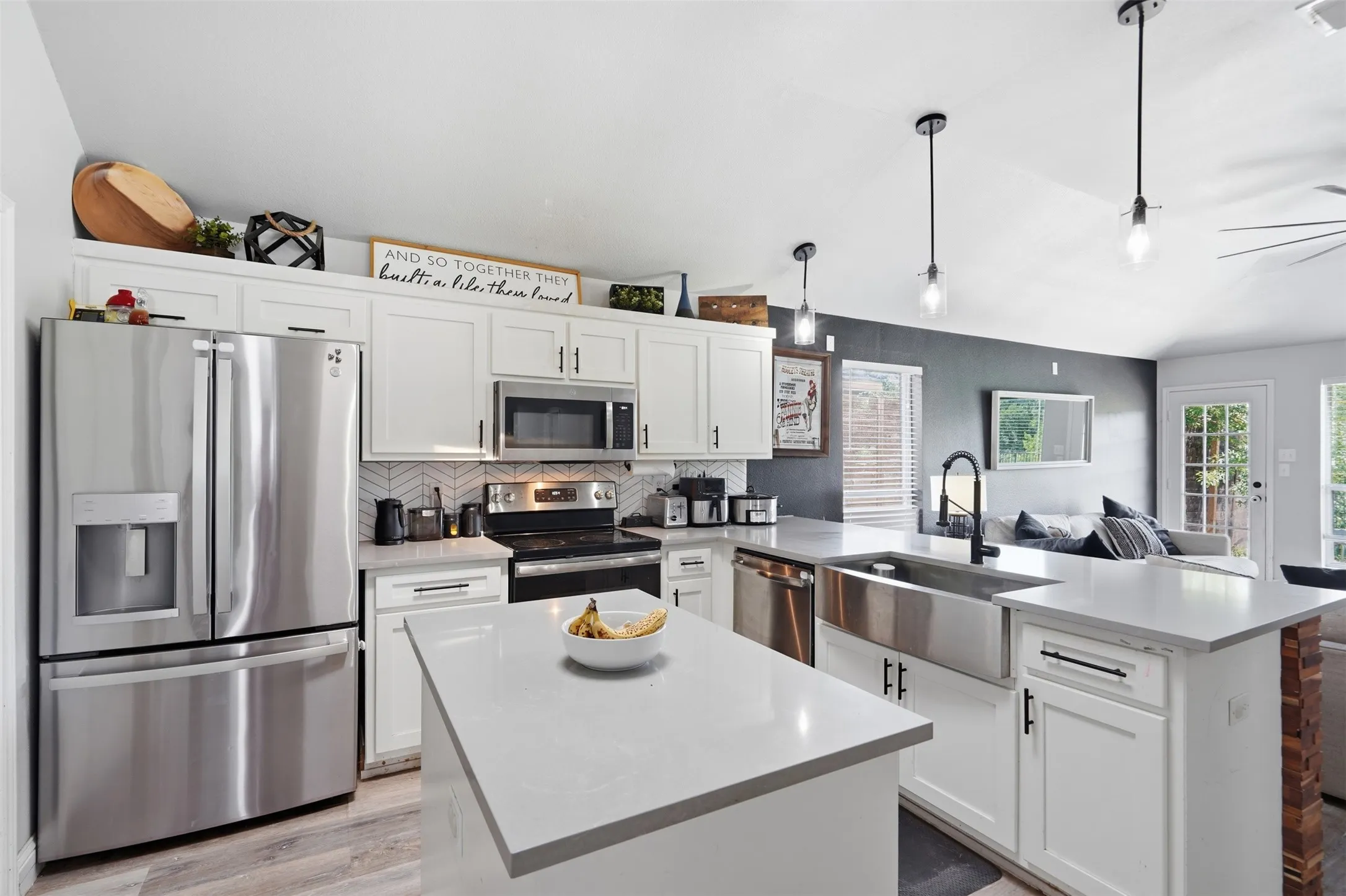 Modern kitchen featuring white cabinetry, light-toned countertops, stainless steel appliances, and a farmhouse-style sink