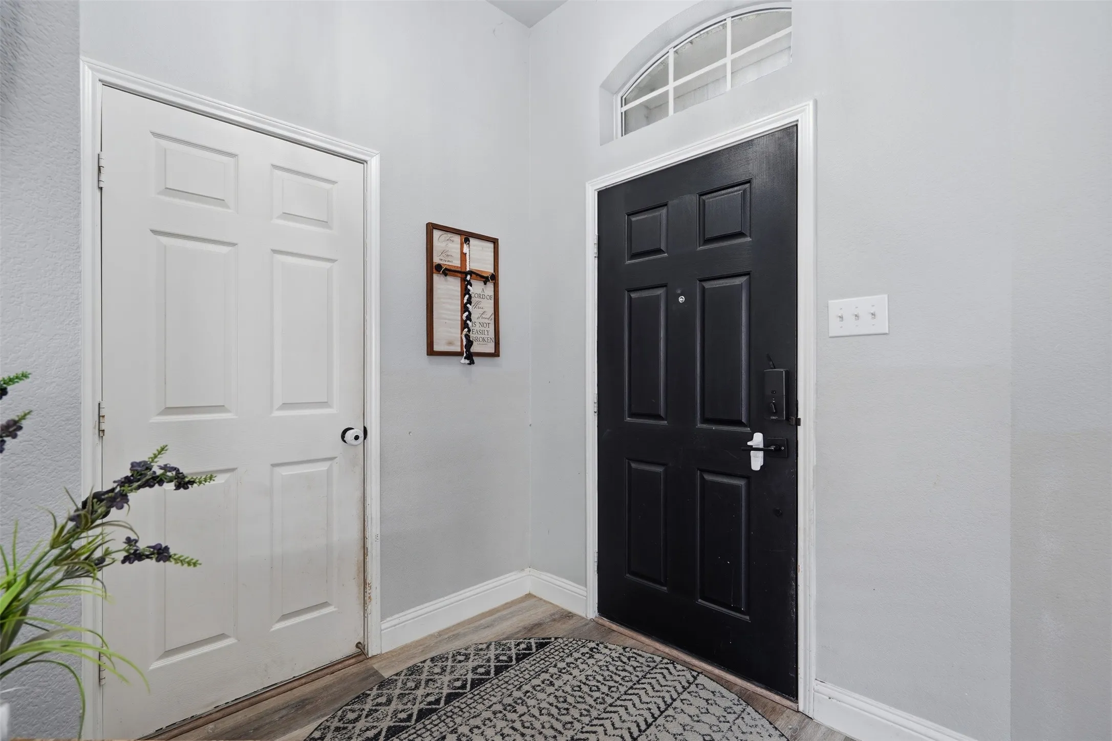 Entryway featuring a paneled black door with an arched transom window above, a white paneled interior door, and wood-finish flooring