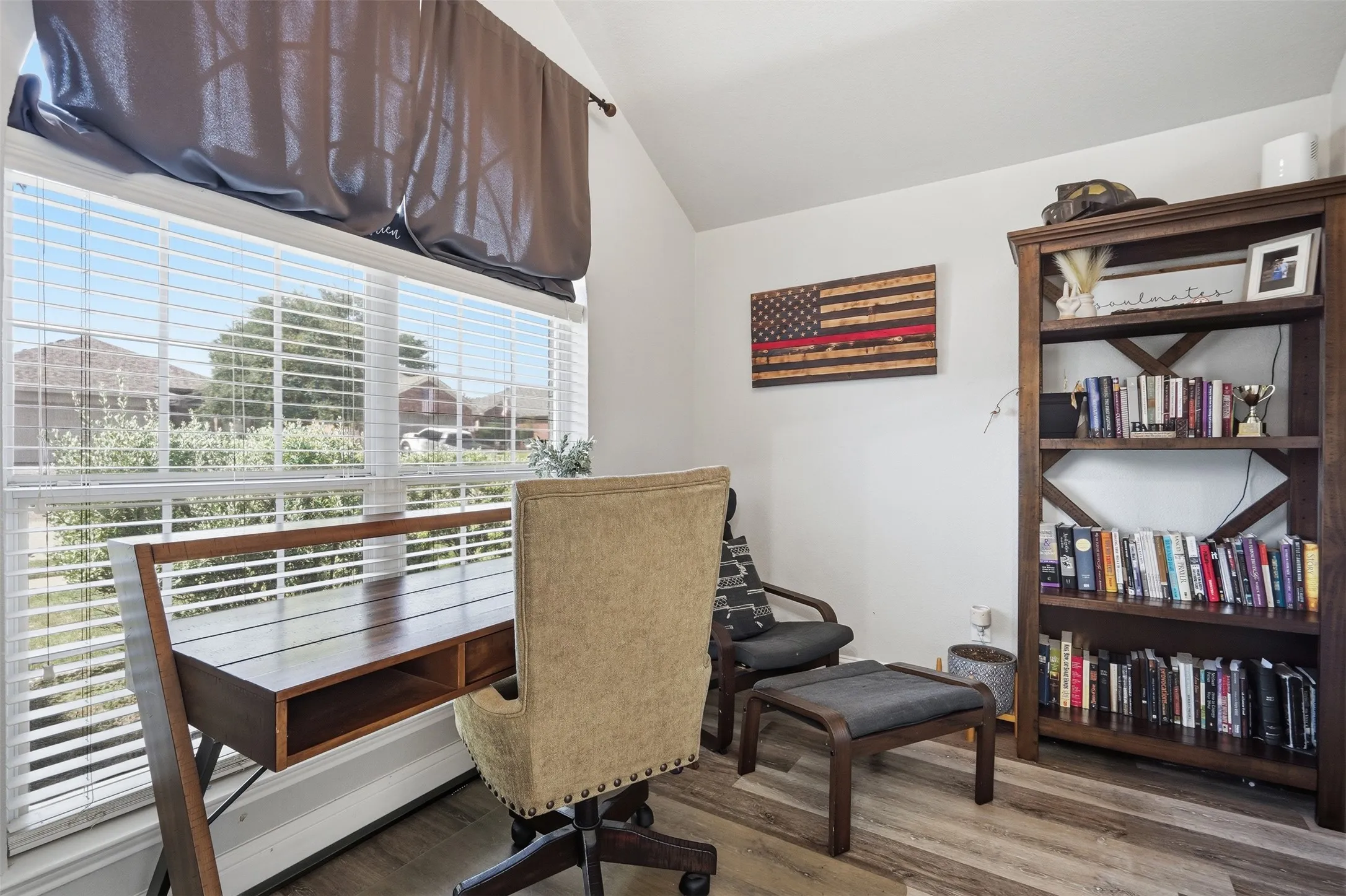 Bright room featuring large windows with blinds, vaulted ceiling, and wood-finish flooring