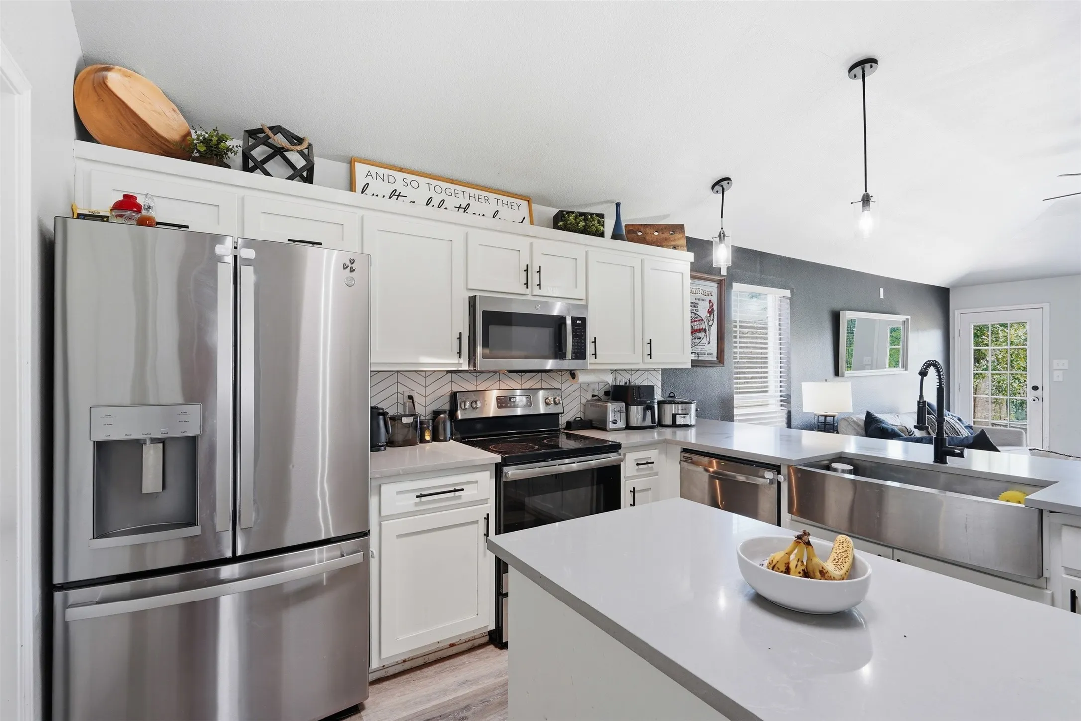 Contemporary kitchen featuring white cabinetry with black hardware, stainless steel appliances, a herringbone tile backsplash, and light-toned countertops