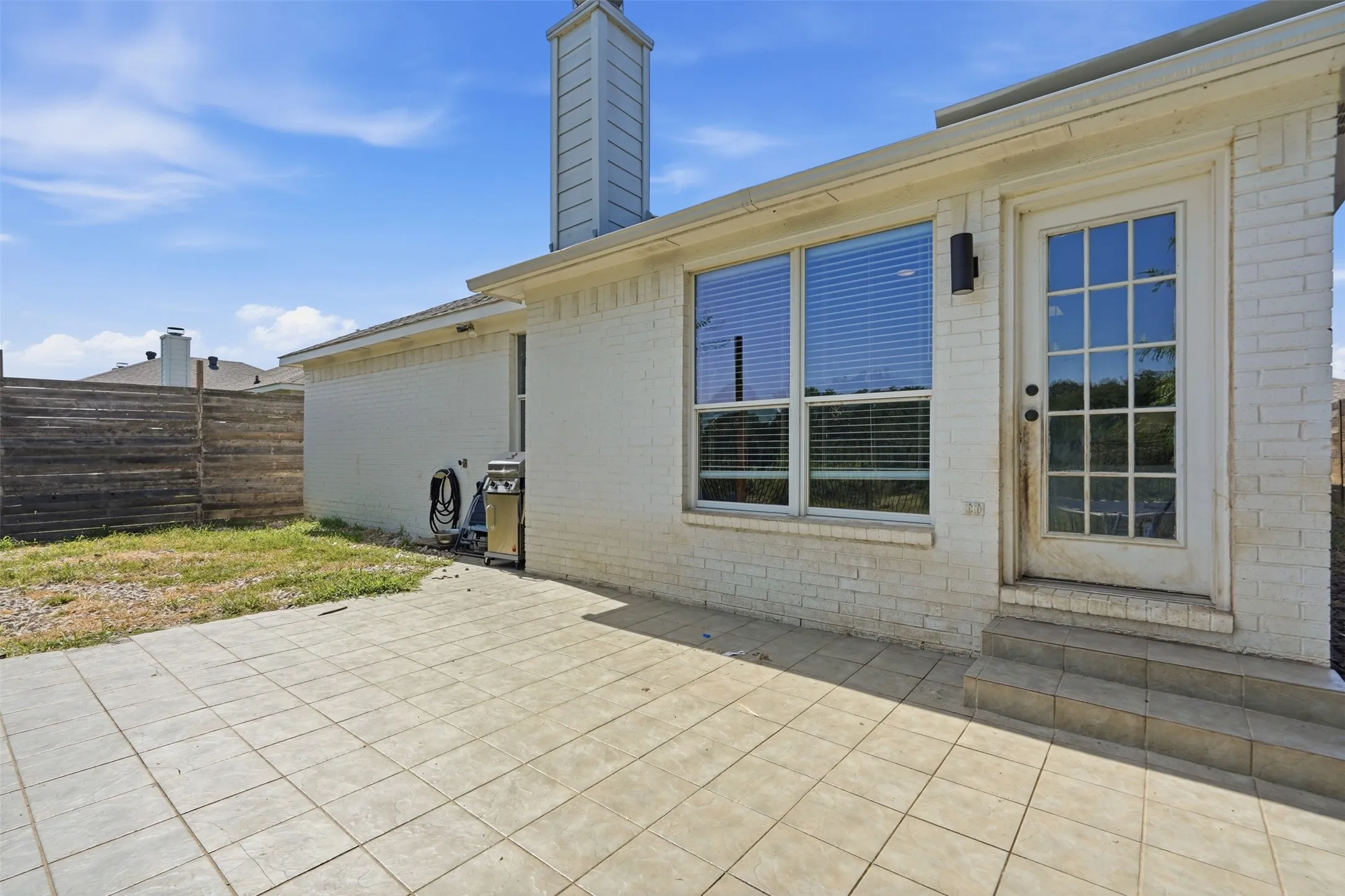 Expansive patio with large format tile pavers, offering direct access to the interior through a glass-paneled door