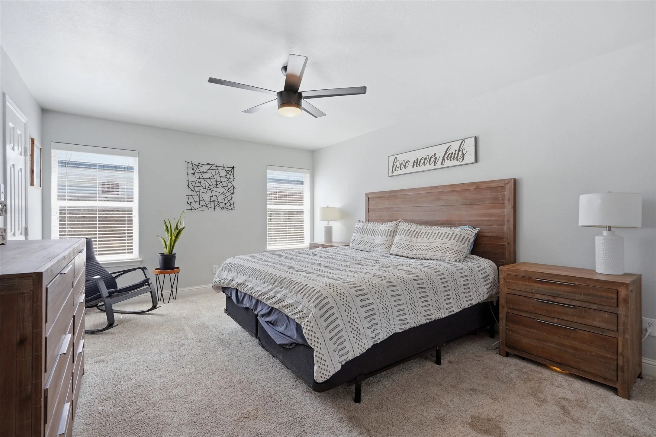 Spacious bedroom featuring light-colored carpeting, multiple windows with blinds, and a ceiling fan with integrated lighting