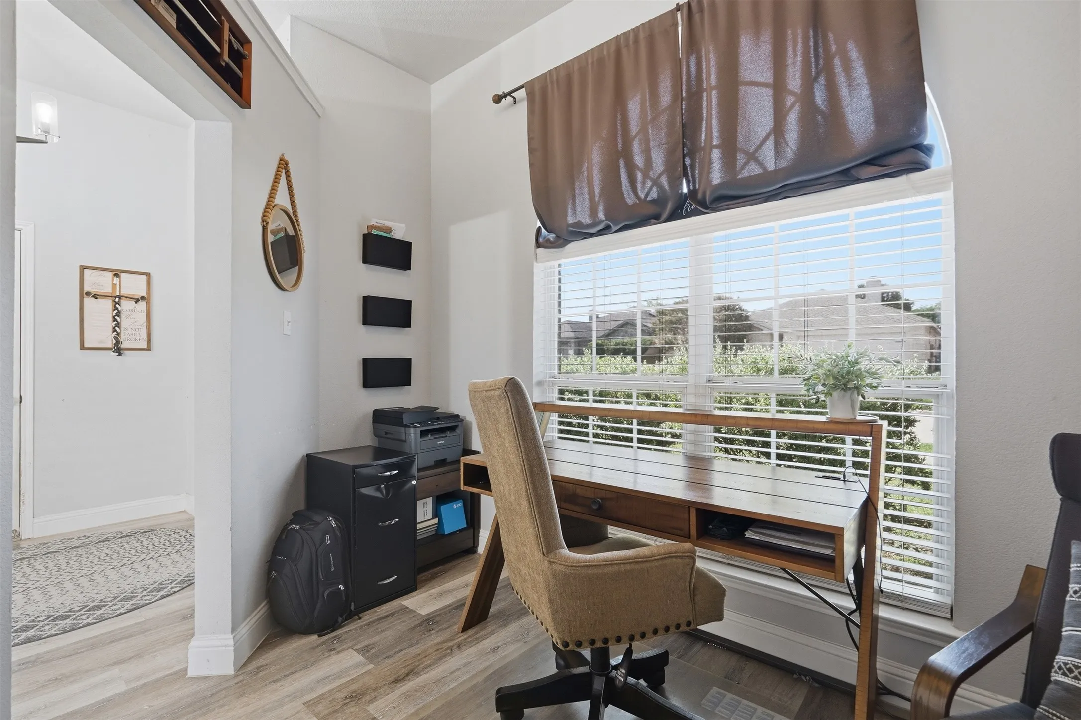 Bright office space featuring wood-finish flooring, a large window with blinds, and white wall finishes