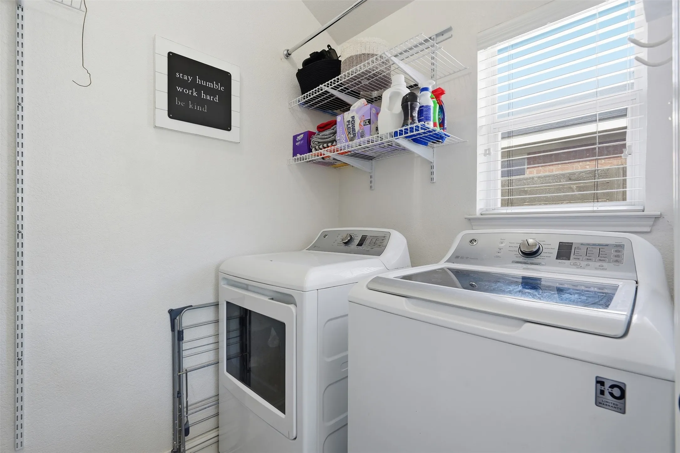 Dedicated laundry area featuring a window with blinds, white shelving, and a built-in hanging rod