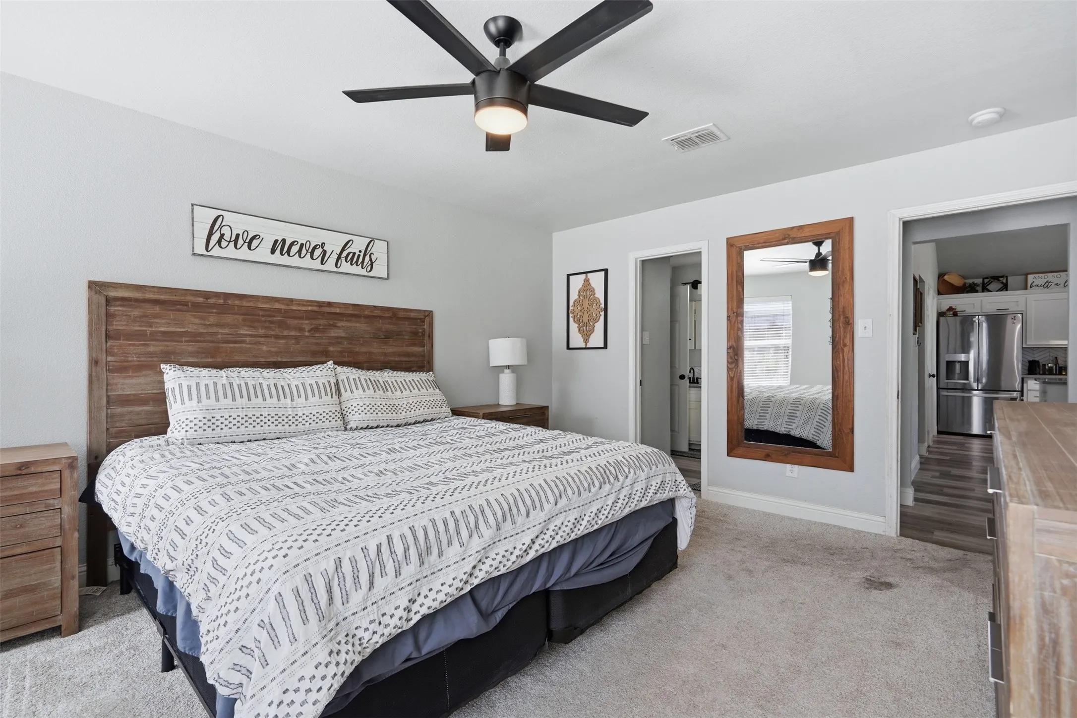 Bedroom featuring light gray wall paint, wood-finish headboard, a ceiling fan with integrated lighting, and light gray carpet flooring
