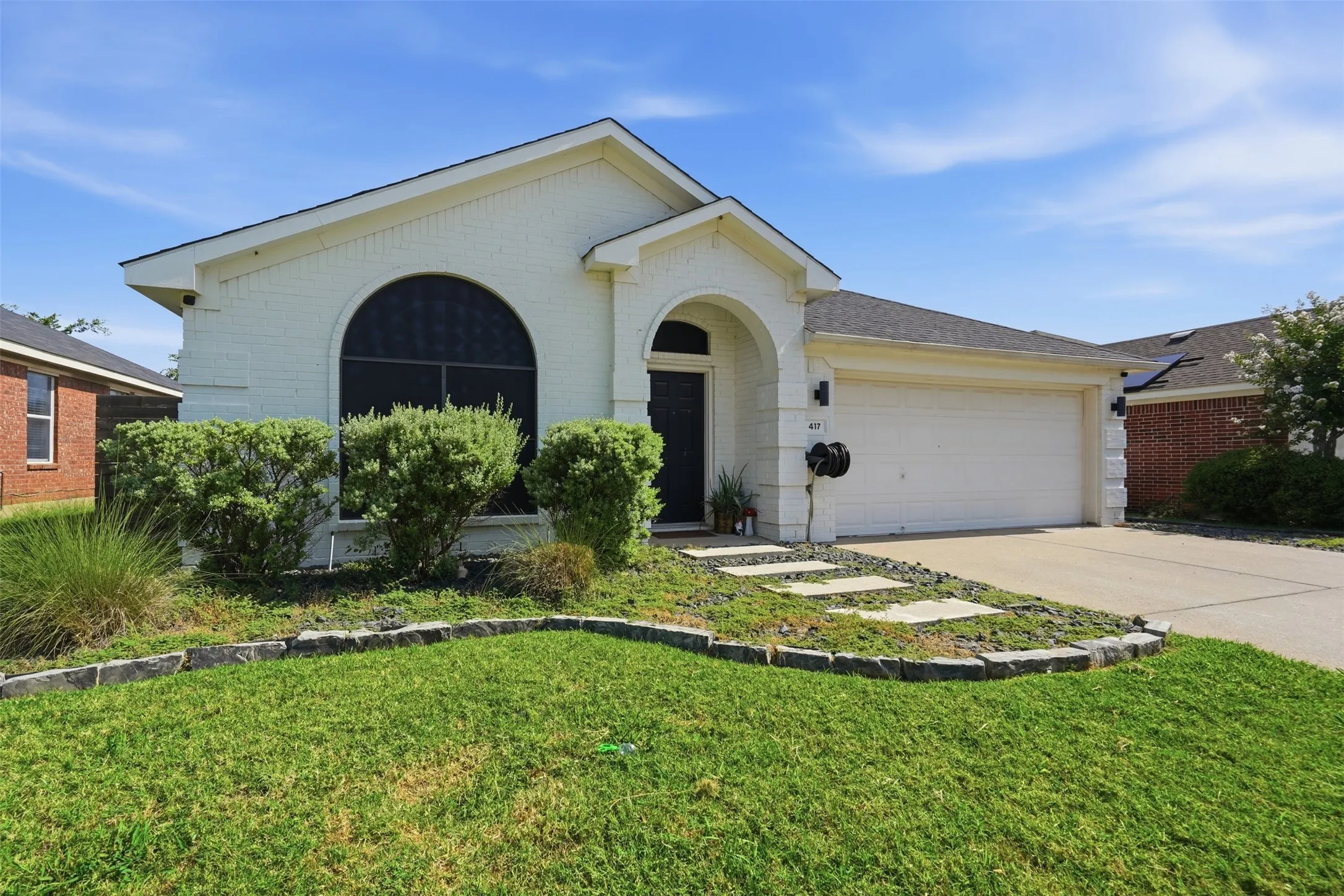 Single-story residence featuring a two-car garage, arched entryways, and a manicured lawn