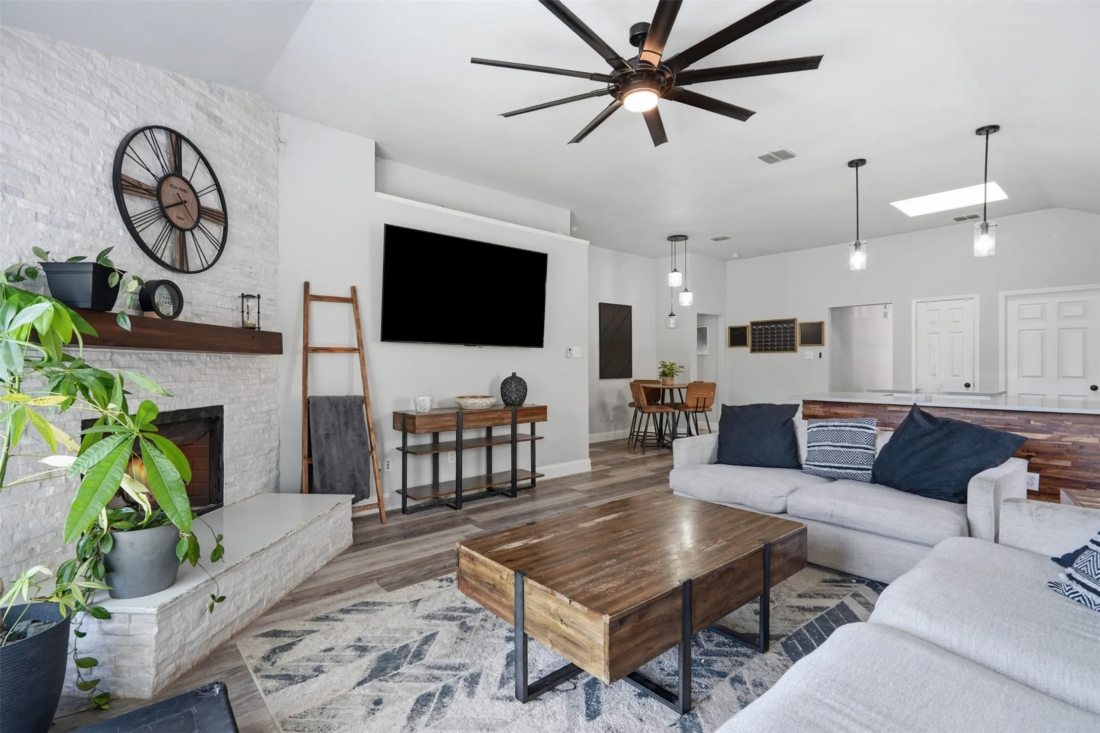 Spacious living area featuring a stone-clad fireplace with a wood mantel, wood-finish flooring, and a contemporary ceiling fan
