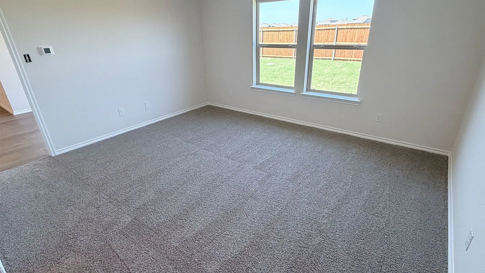Spacious bedroom featuring neutral carpet flooring, large dual-pane windows with natural light, and white wall finishes throughout