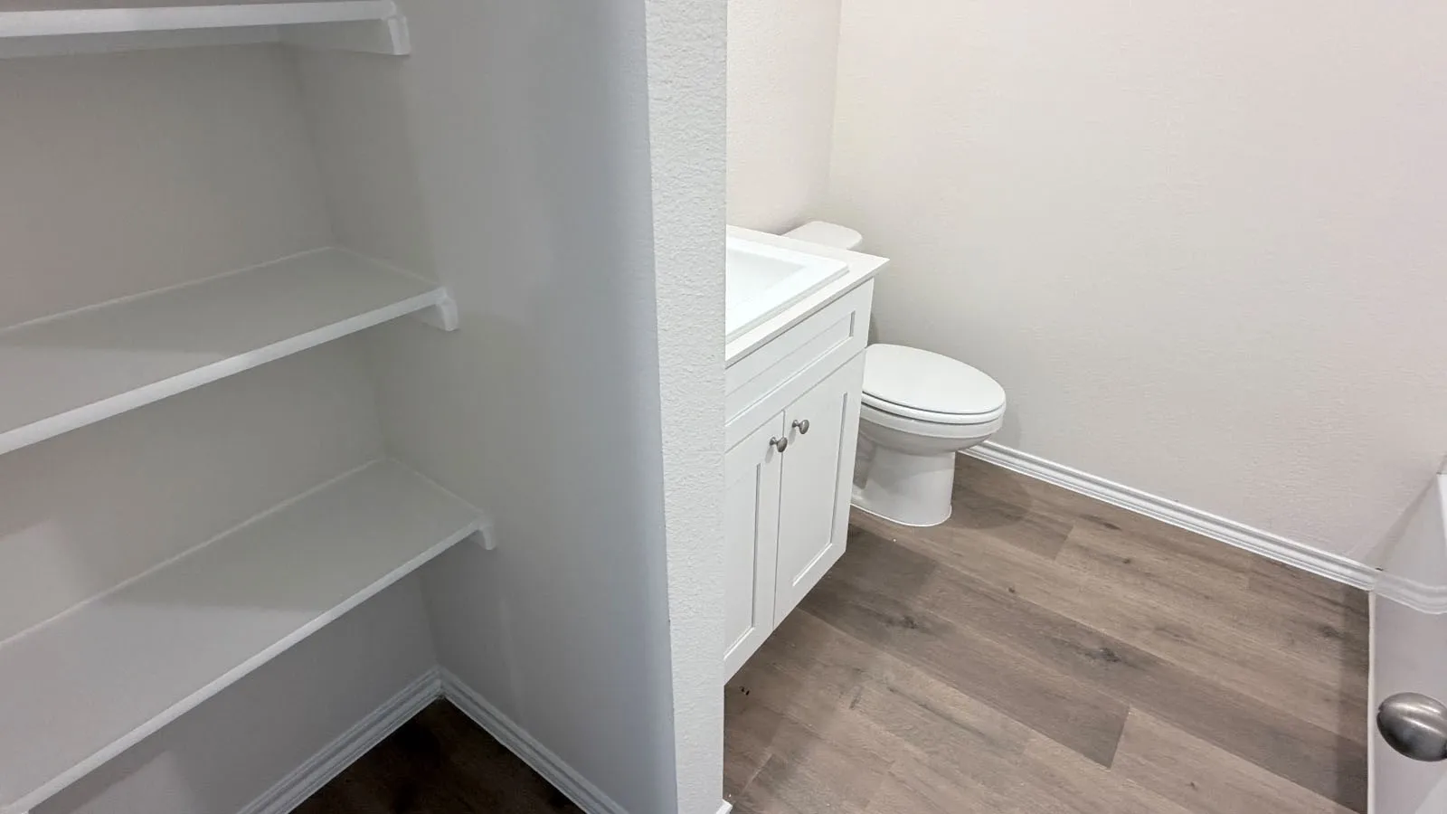 Compact bathroom featuring white cabinetry with integrated sink vanity, ceramic toilet, and wood-finish flooring throughout