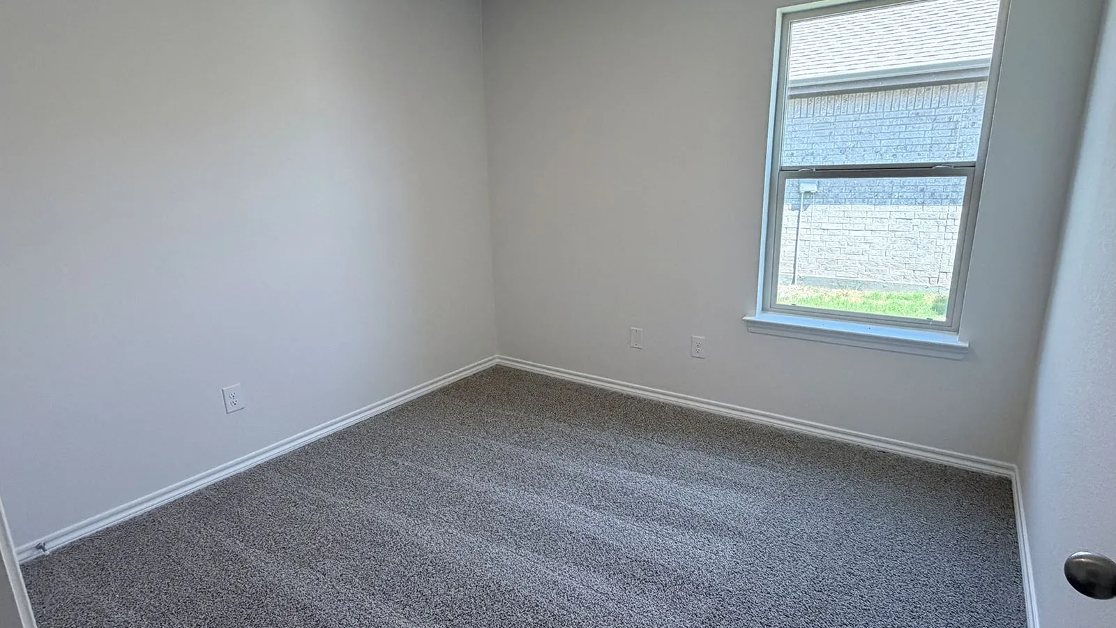Bright corner bedroom featuring neutral wall finishes, expansive natural light from a large double-hung window, and soft gray carpeting throughout