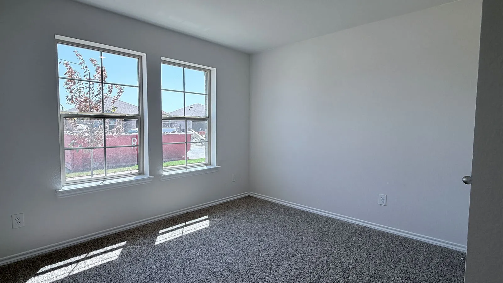 Bright corner bedroom featuring dual large windows with grid detailing, abundant natural light, neutral wall finishes, and carpet flooring throughout