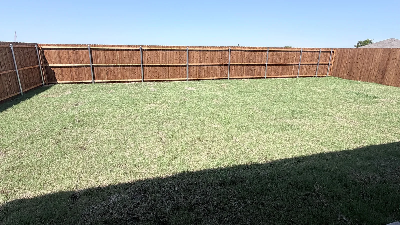 Spacious fenced backyard with mature lawn and sturdy wood-finish perimeter fencing, offering privacy and ample outdoor space