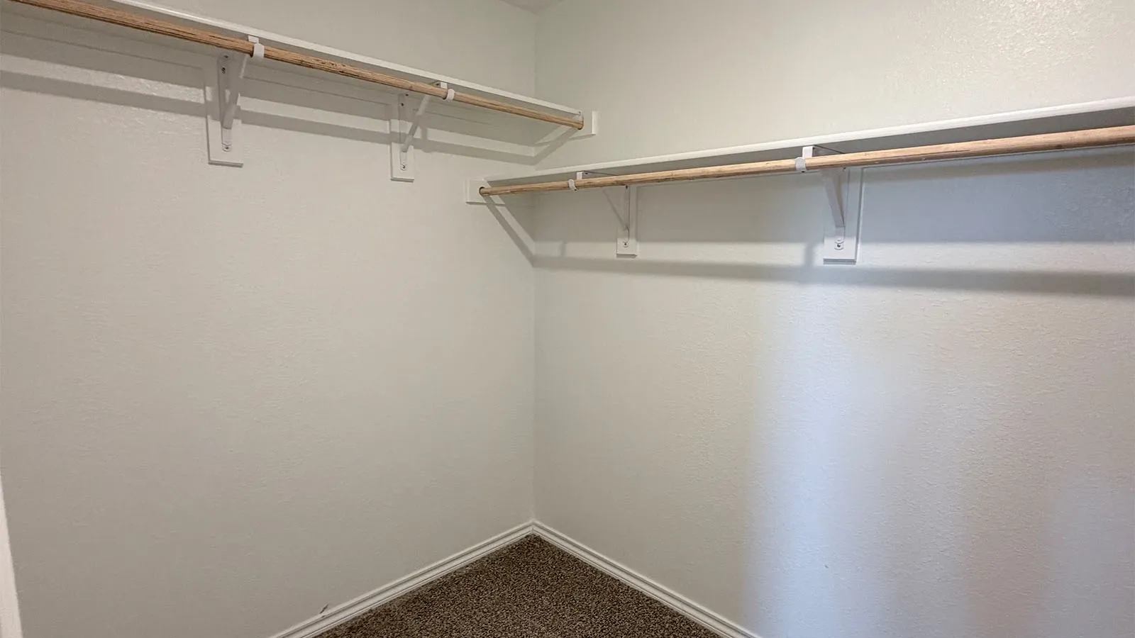 Closet space featuring neutral-toned walls, carpeting, and multiple storage rods