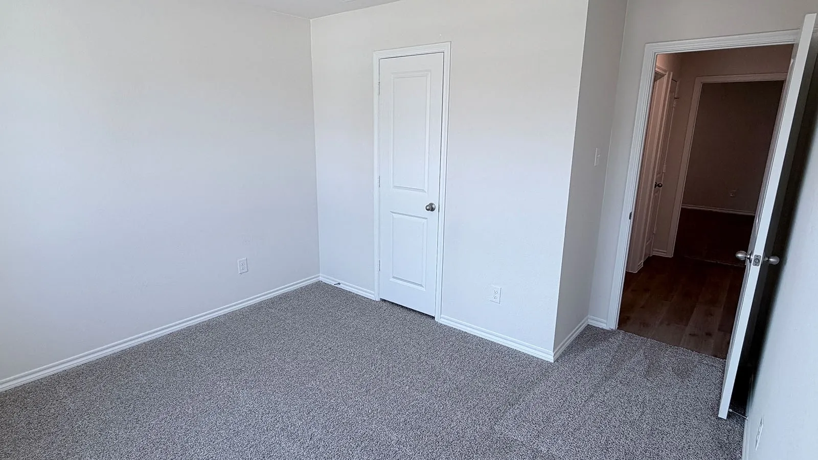 Spacious bedroom with neutral wall finishes, carpeted flooring, and multiple entry points including a white six-panel closet door and secondary access to adjacent spaces