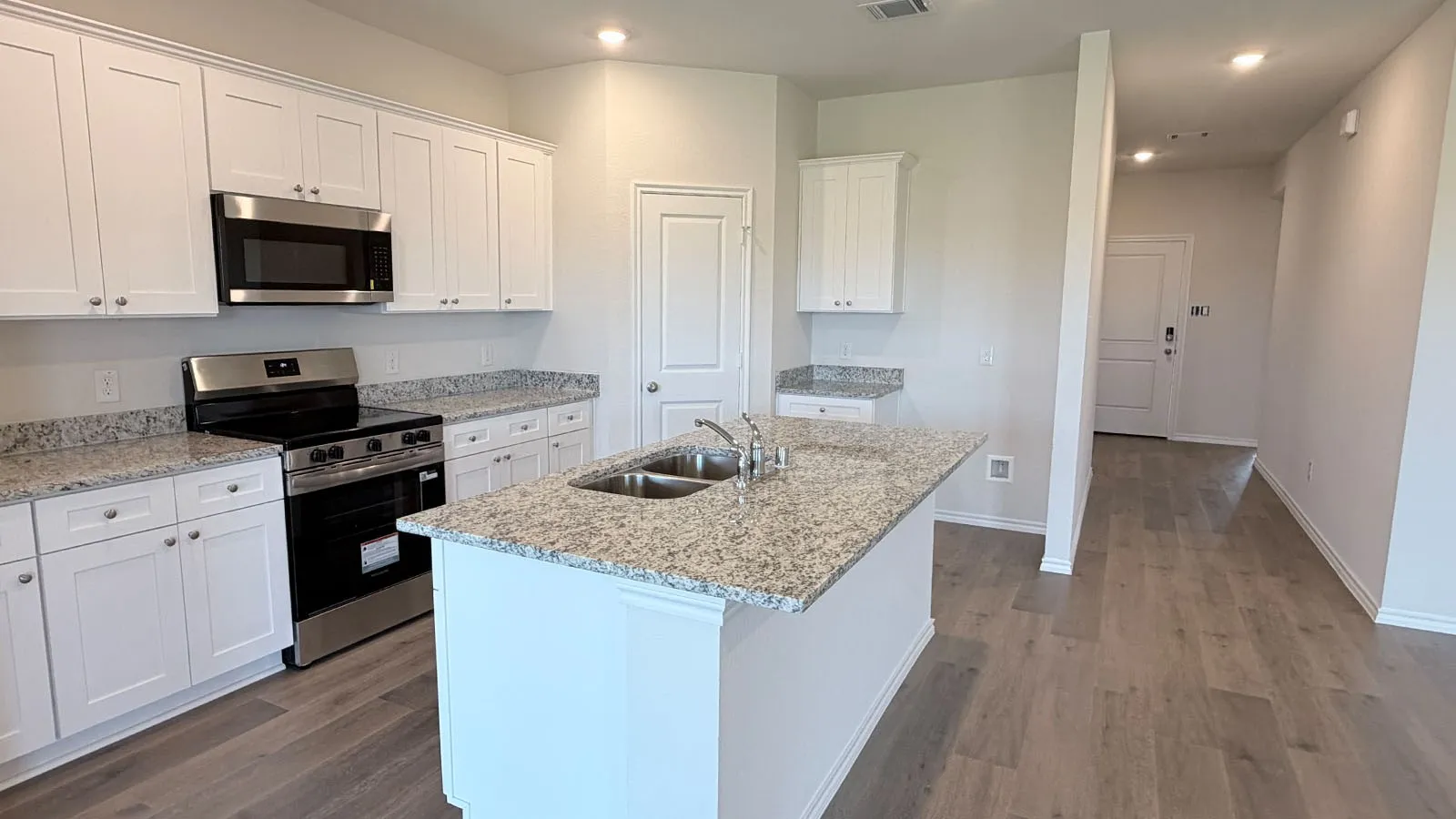Modern kitchen featuring white shaker cabinetry, stainless steel appliances, granite countertops, a center island with breakfast bar seating, and wood-finish flooring throughout the open-concept living area