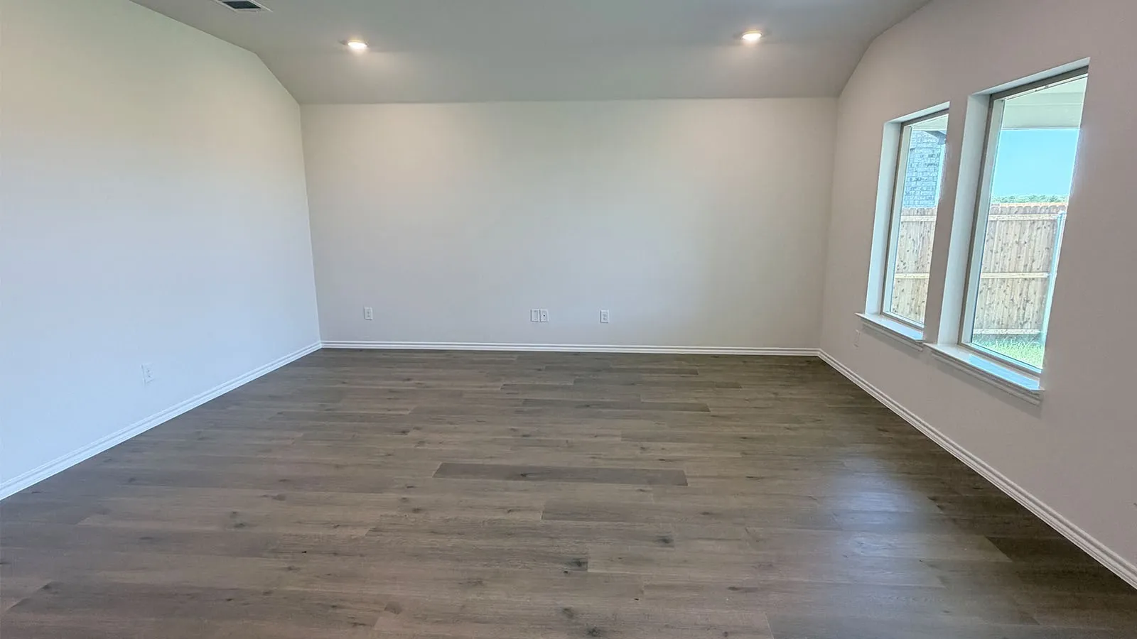 Wood-finish flooring with recessed lighting, complemented by multiple windows and crisp white walls