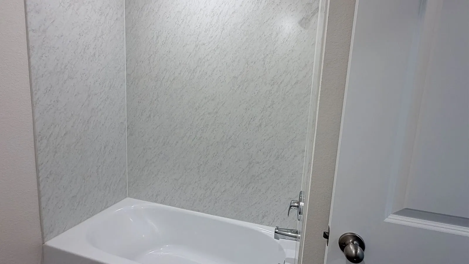 Modern bathroom featuring a white acrylic soaking tub, marble-finish wall surround, chrome single-handle faucet, and frameless glass enclosure with polished hardware