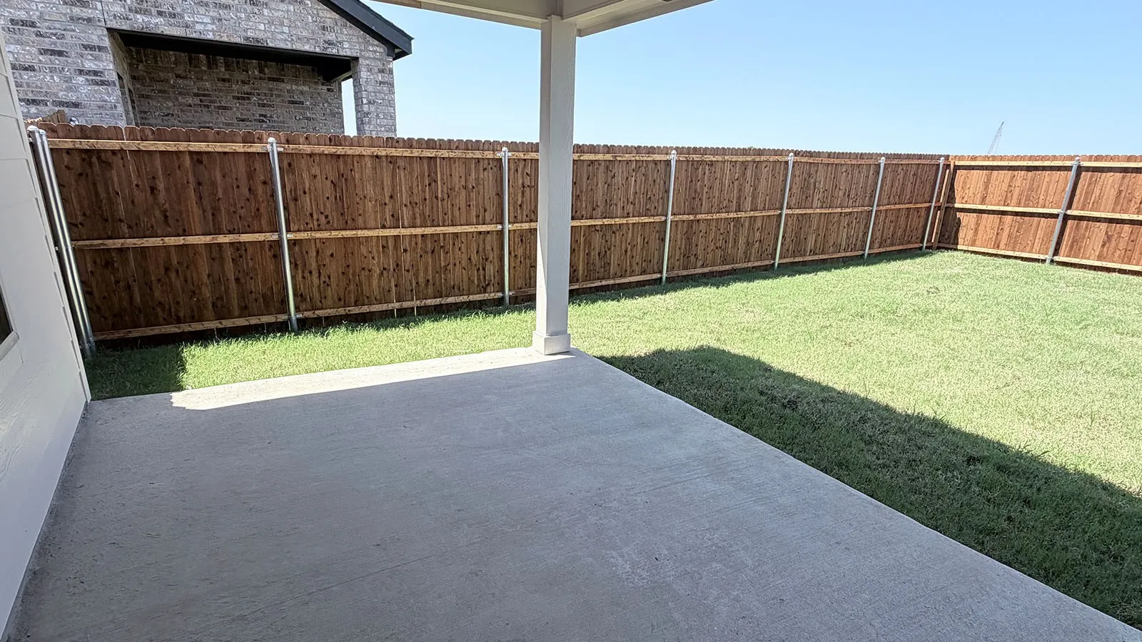 Expansive covered patio with concrete flooring overlooking a fenced backyard featuring manicured lawn and wood-finish privacy fencing