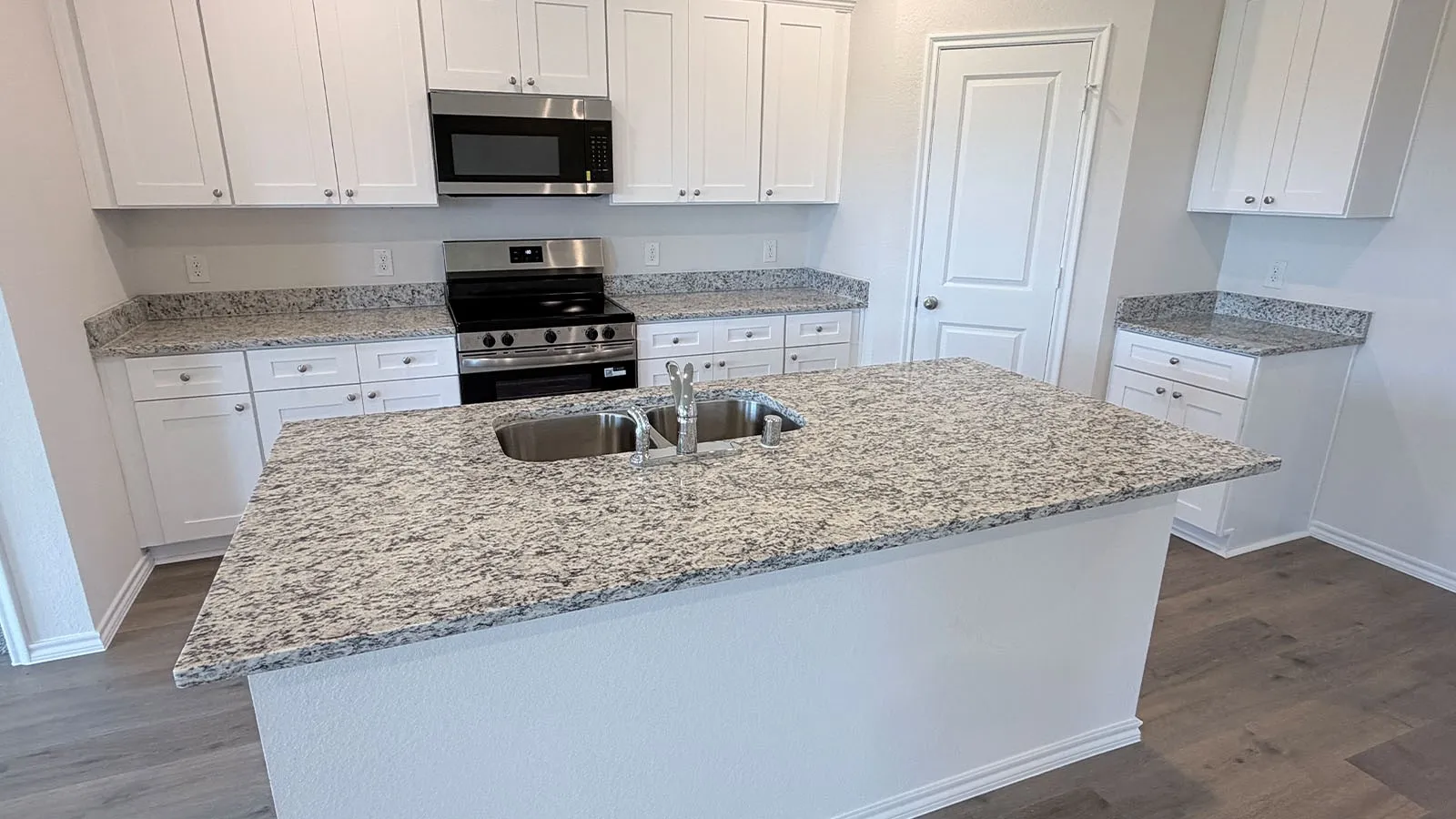 Chef's kitchen featuring custom white cabinetry, stainless steel appliances, dual undermount sinks, and expansive granite-style countertops with waterfall island edge