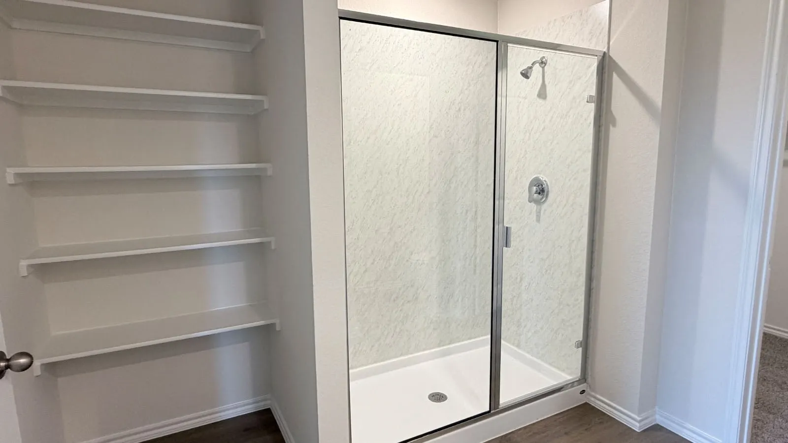Built-in shelving, glass-enclosed shower with a chrome showerhead, and a white shower pan