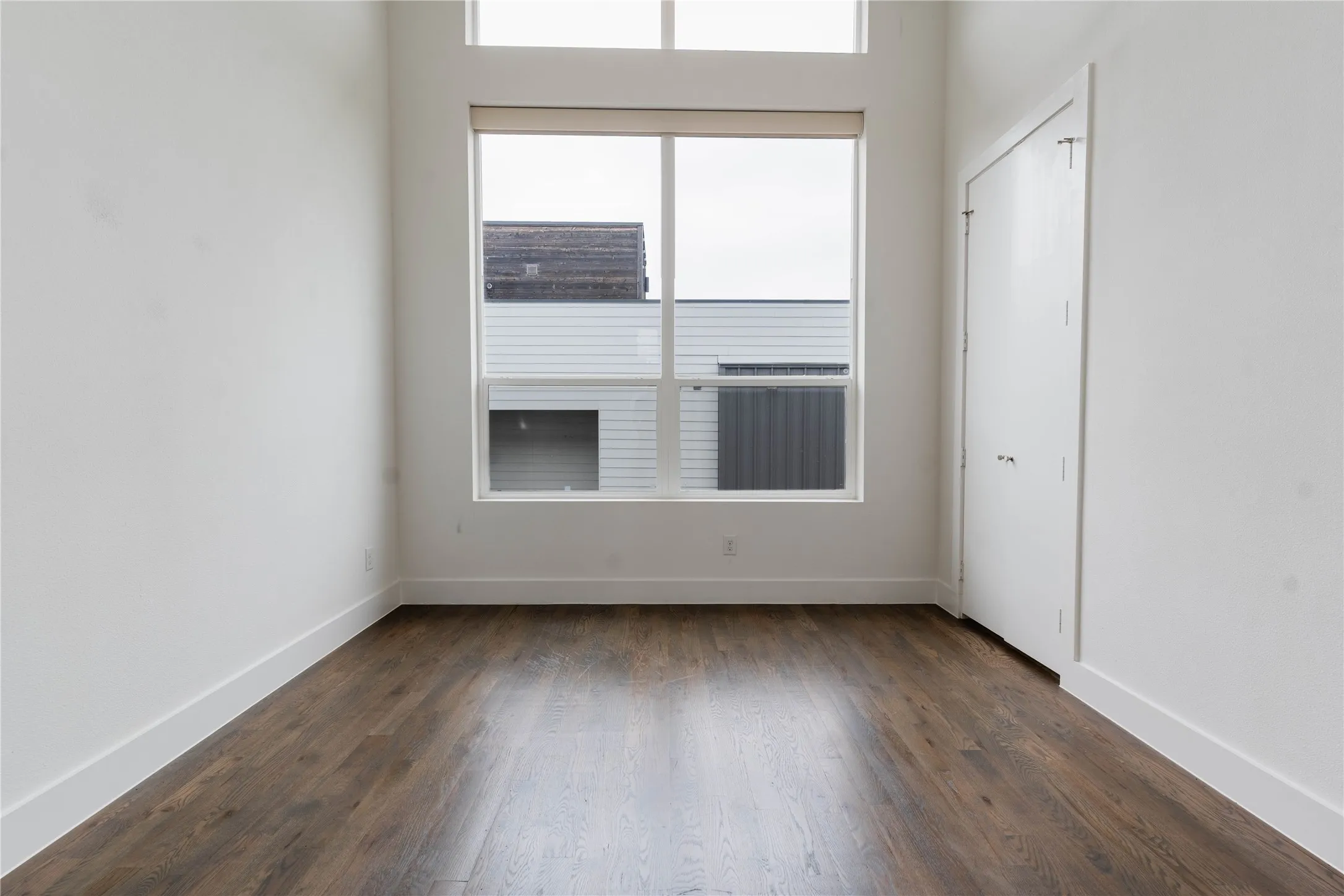 Room with wood-finish flooring, white walls, and a large window featuring a transom above