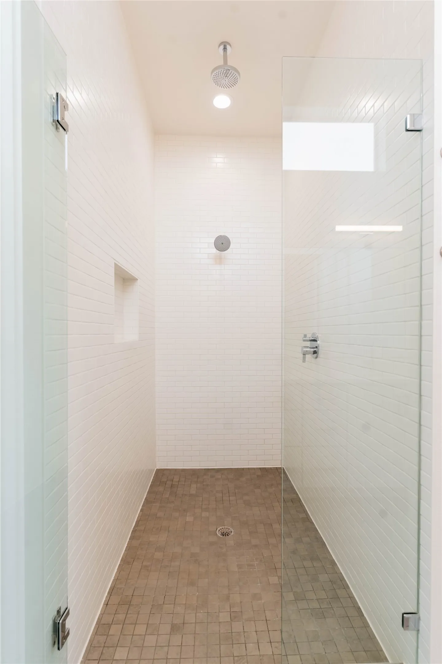 Spacious shower enclosure featuring white subway tile walls, a rain showerhead, a wall-mounted shower control, a built-in shower niche, and a frameless glass door