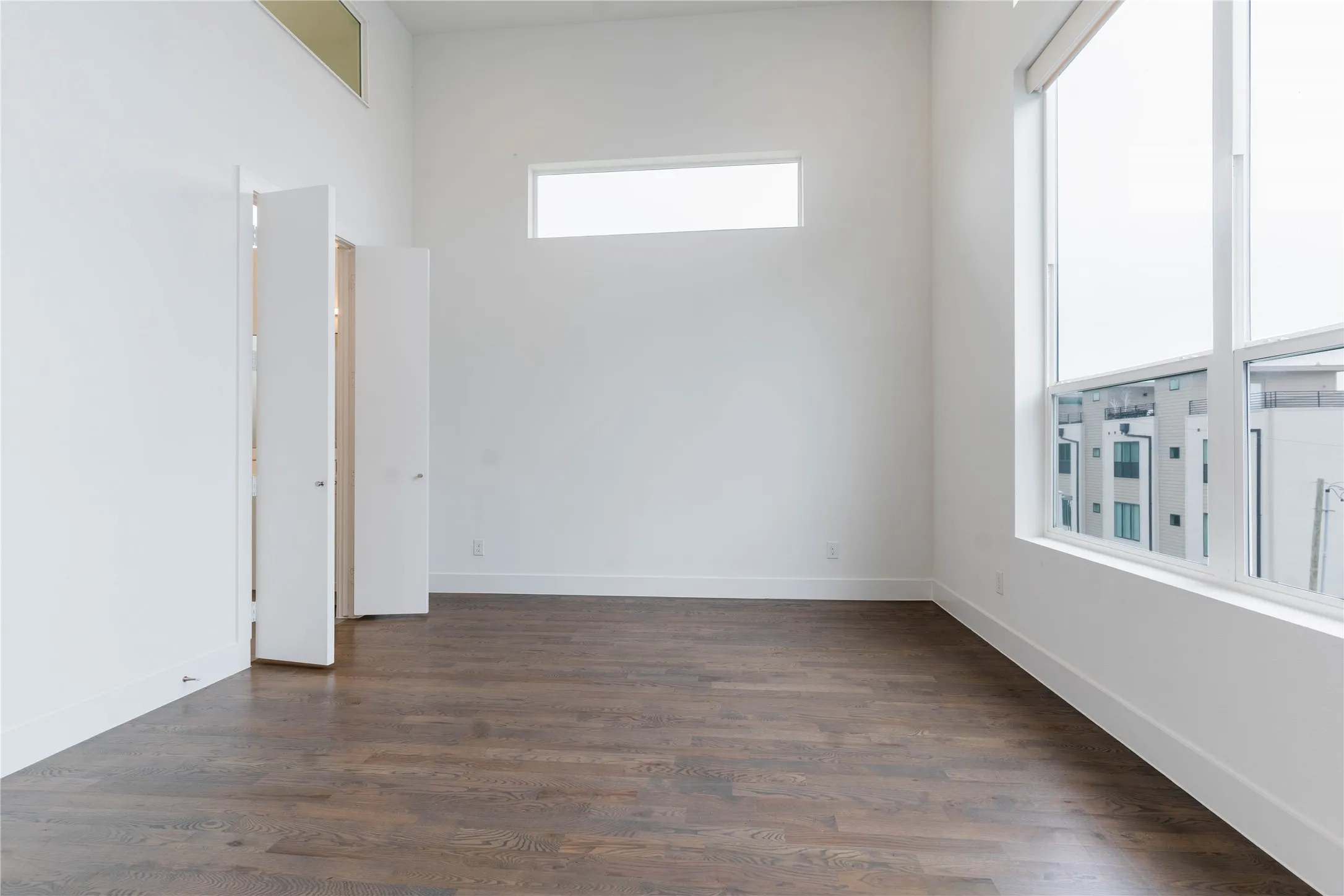 Spacious room featuring high ceilings, wood-finish flooring, and expansive windows with roller shades