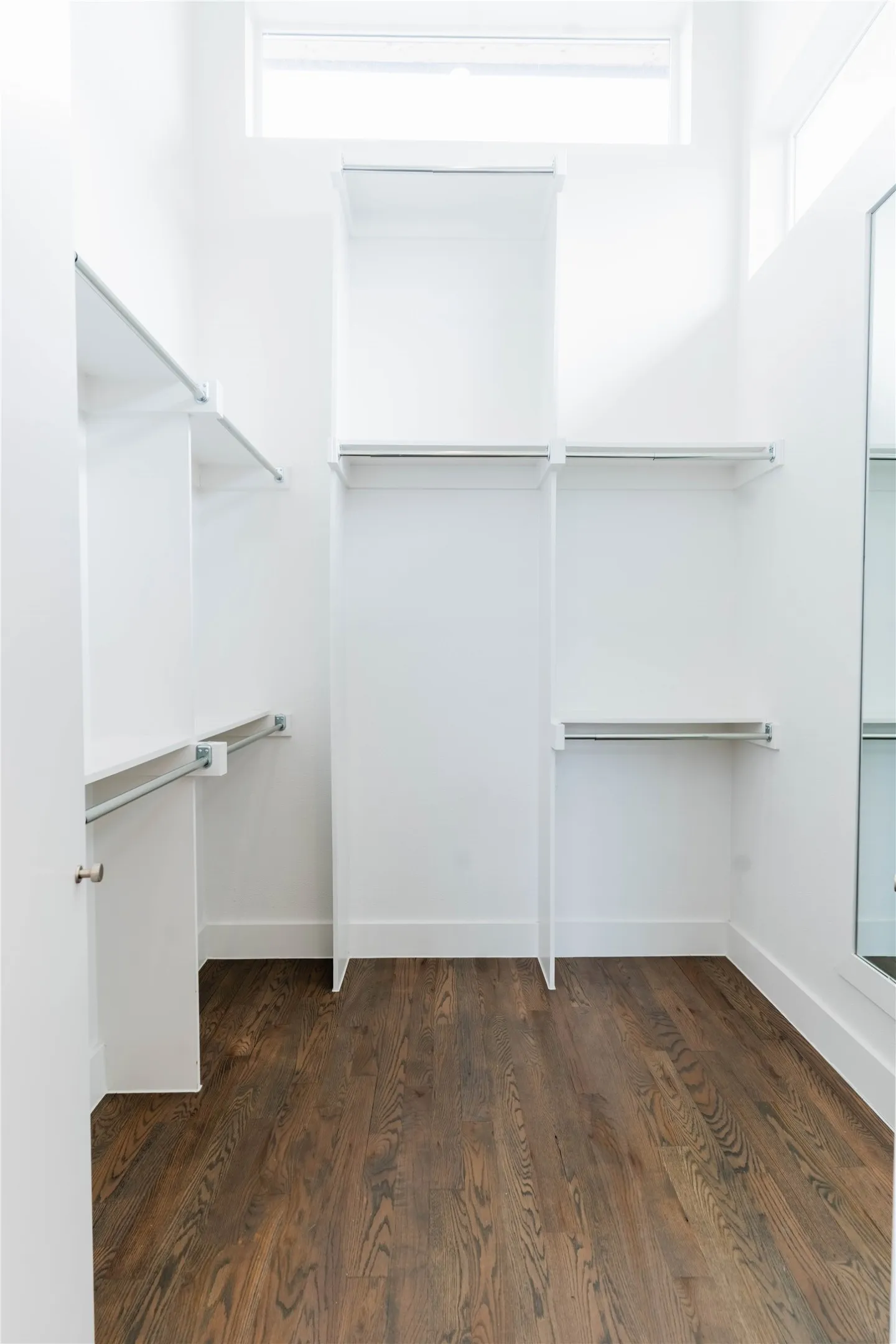 Spacious walk-in closet featuring wood-finish flooring, white built-in shelving, and multiple clothing rods