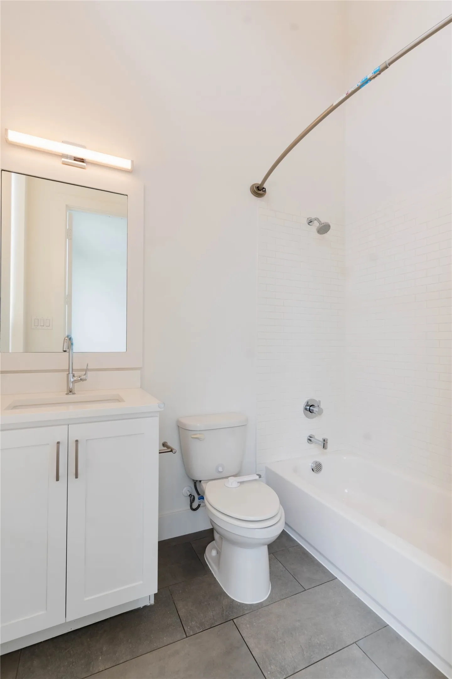 Bathroom featuring a white vanity with a rectangular sink, a contemporary wall-mounted light fixture, and a bathtub with white subway tile surround