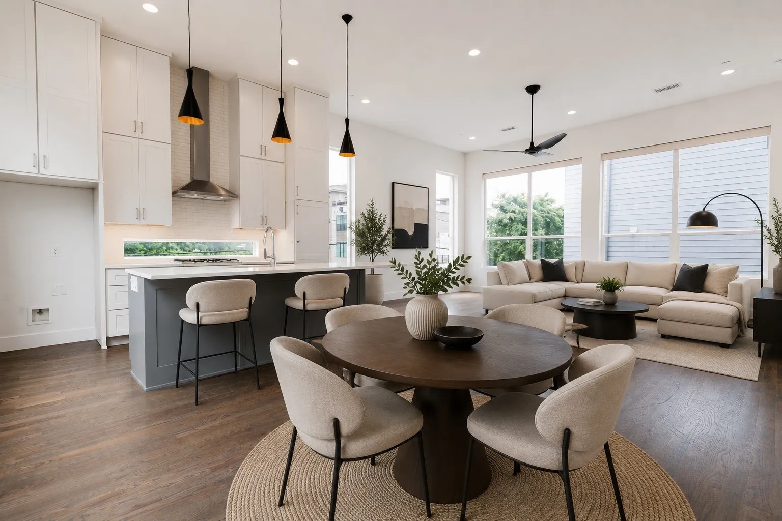 Open-concept living space featuring wood-finish flooring, a contemporary kitchen island with seating, white shaker-style cabinetry, and large windows
