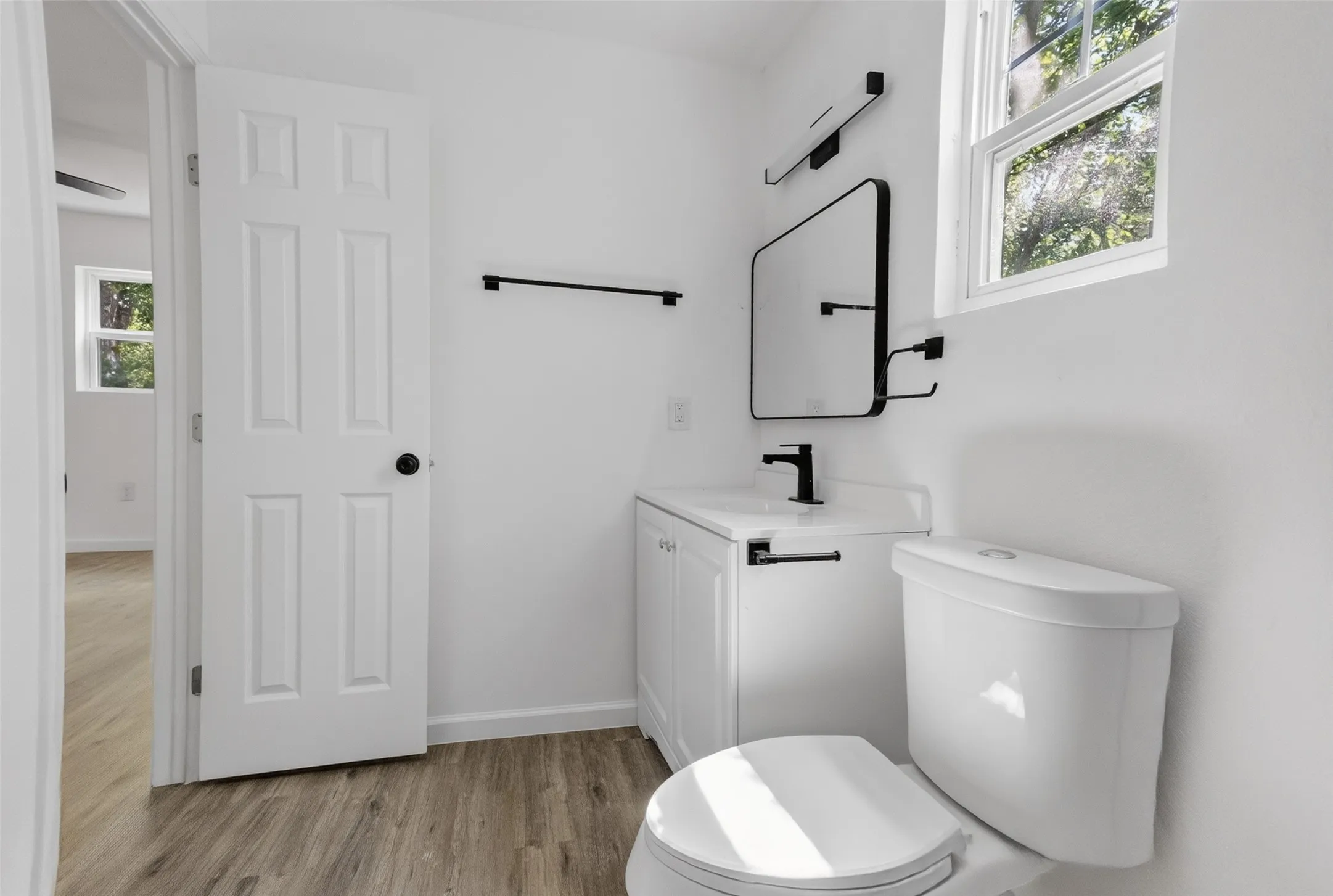 Bathroom featuring a white vanity with integrated sink, black fixtures, rectangular mirror, and wood-finish flooring