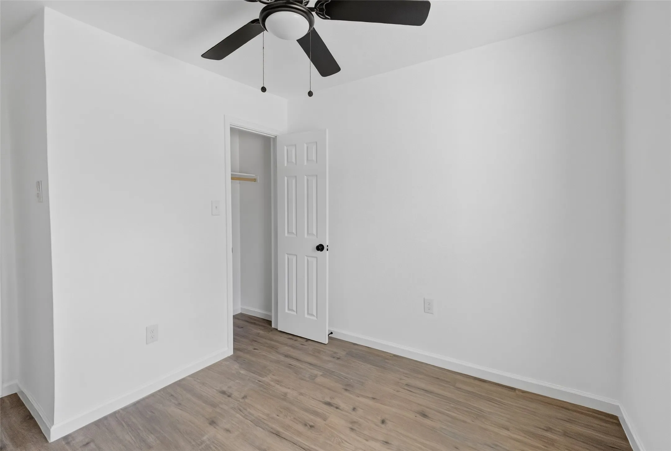 Interior room featuring wood-finish flooring, white walls, and a ceiling fan with integrated lighting