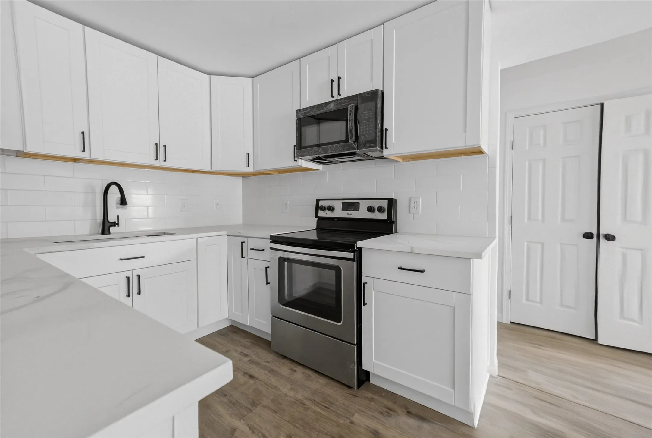 Modern kitchen featuring white shaker cabinetry, stainless steel appliances, a subway tile backsplash, light-toned countertops, and wood-finish flooring