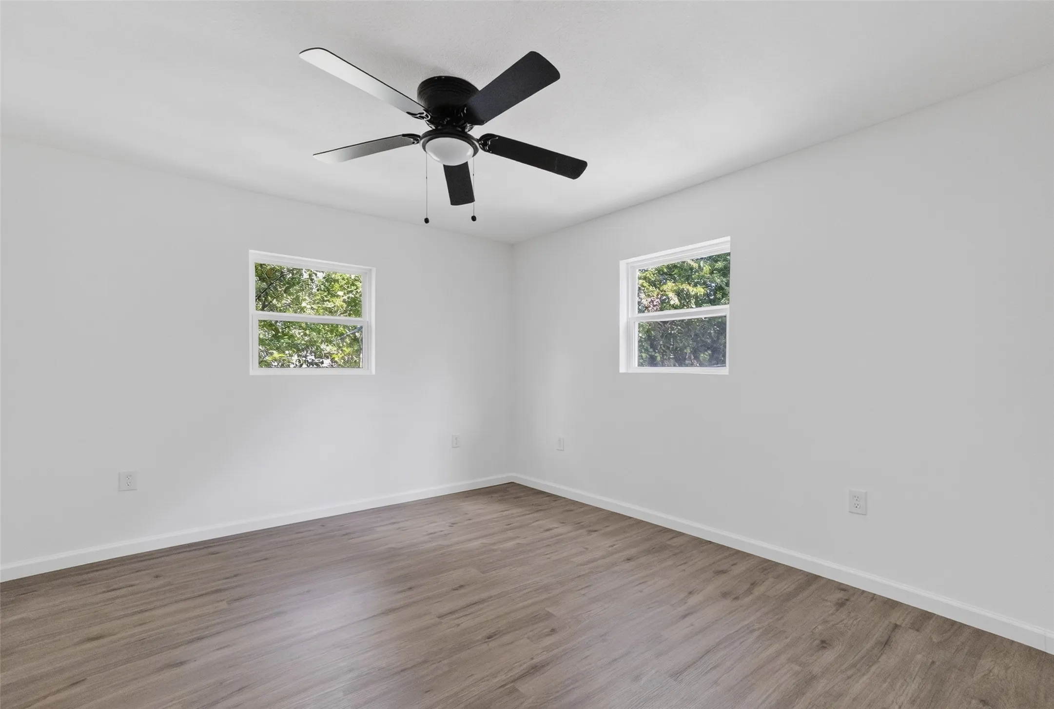 Room featuring wood-finish flooring, white walls, and a ceiling fan with integrated lighting
