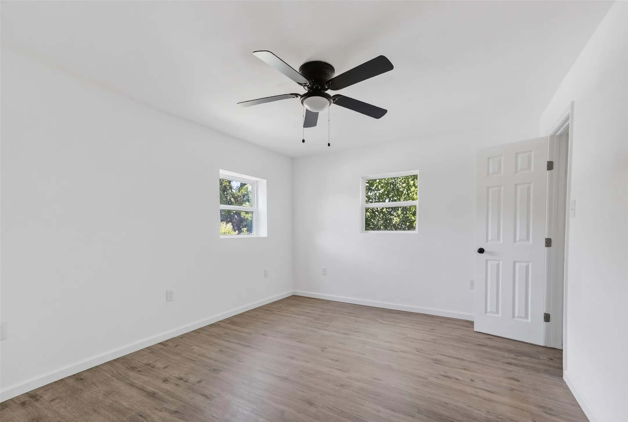 Bright interior space featuring wood-finish flooring, white walls, and a black ceiling fan
