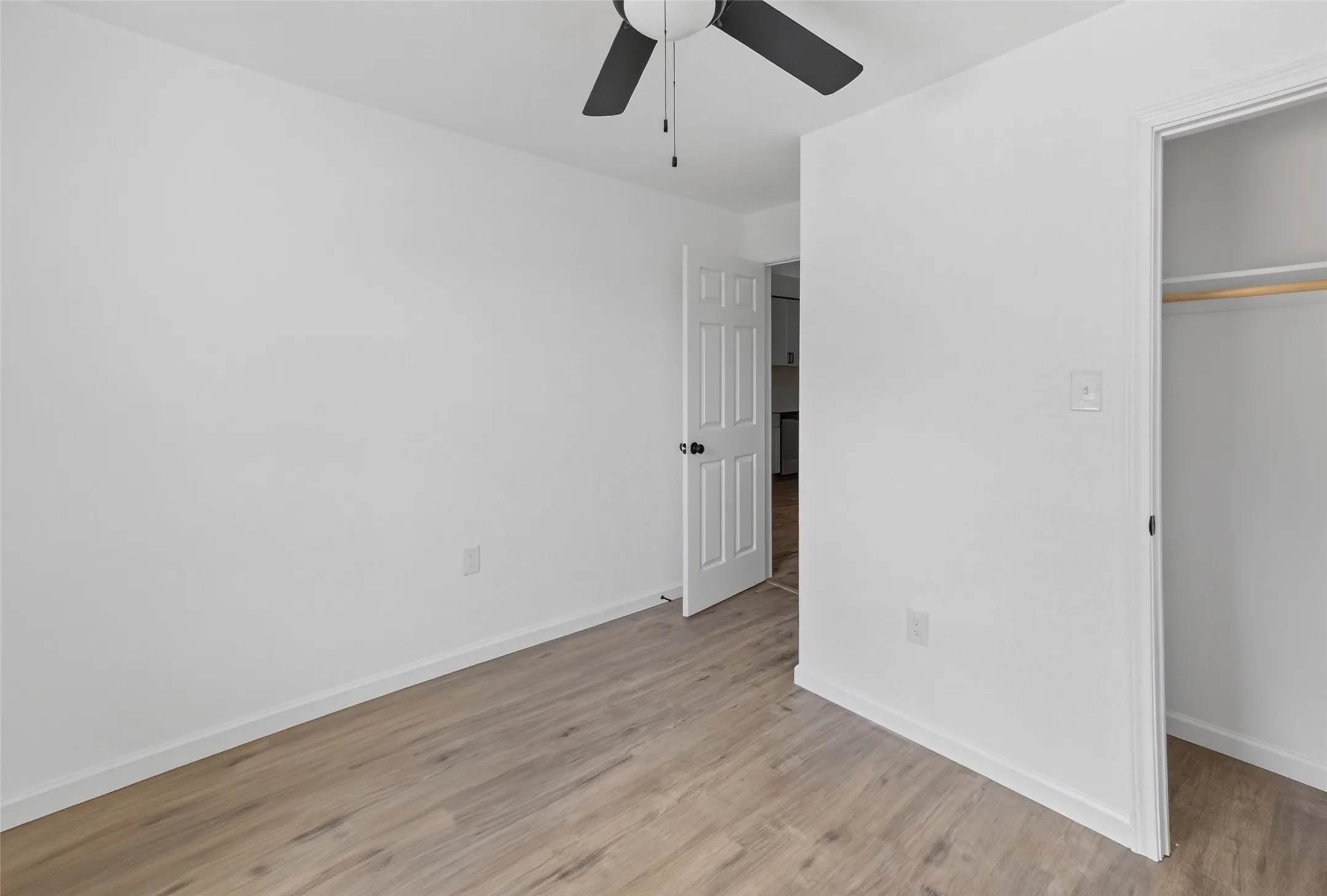 Room featuring light wood-finish flooring, white painted walls, and a ceiling fan with dark blades