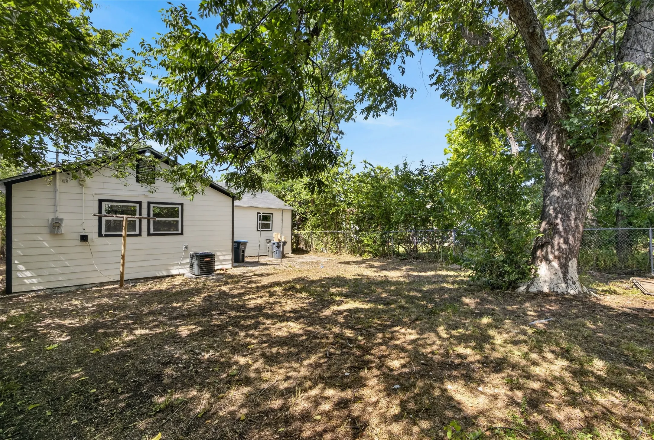 Expansive backyard featuring a large tree, a chain-link fence, and a white-sided building with black-trimmed windows