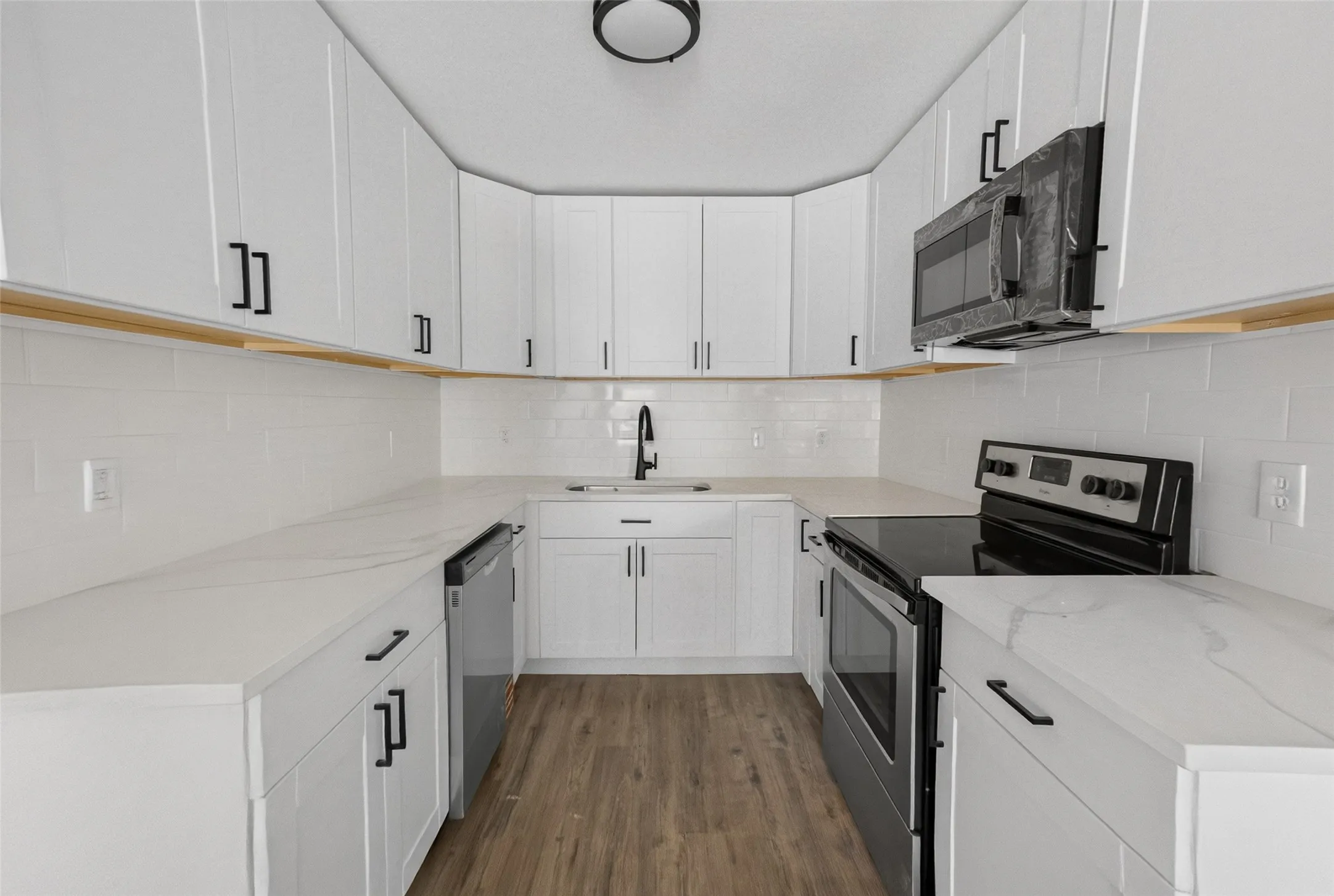 U-shaped kitchen featuring white cabinetry with black hardware, white subway tile backsplash, light-toned countertops, and wood-finish flooring