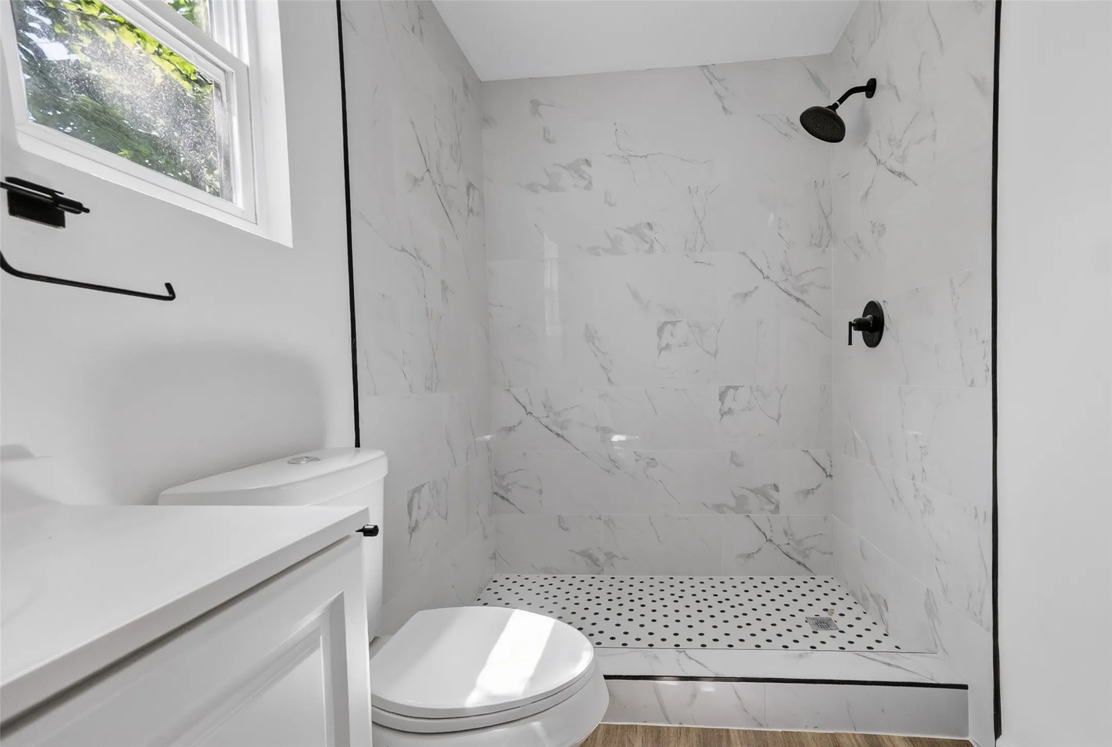 Bathroom featuring a stand-up shower with white marble-look subway tile surround, matte black fixtures, and a black and white mosaic tile shower pan