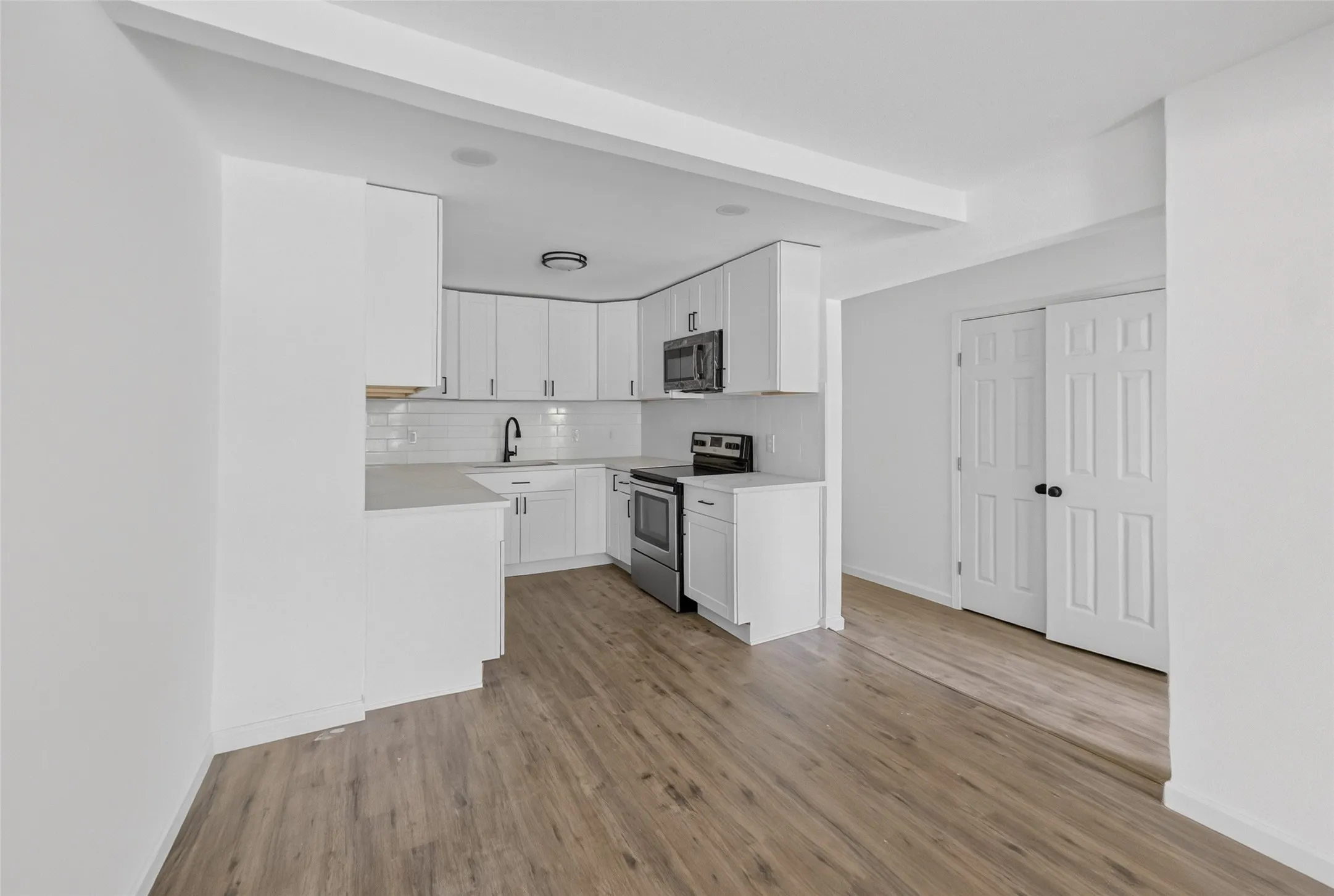 Modern kitchen featuring white cabinetry, subway tile backsplash, stainless steel appliances, and wood-finish flooring