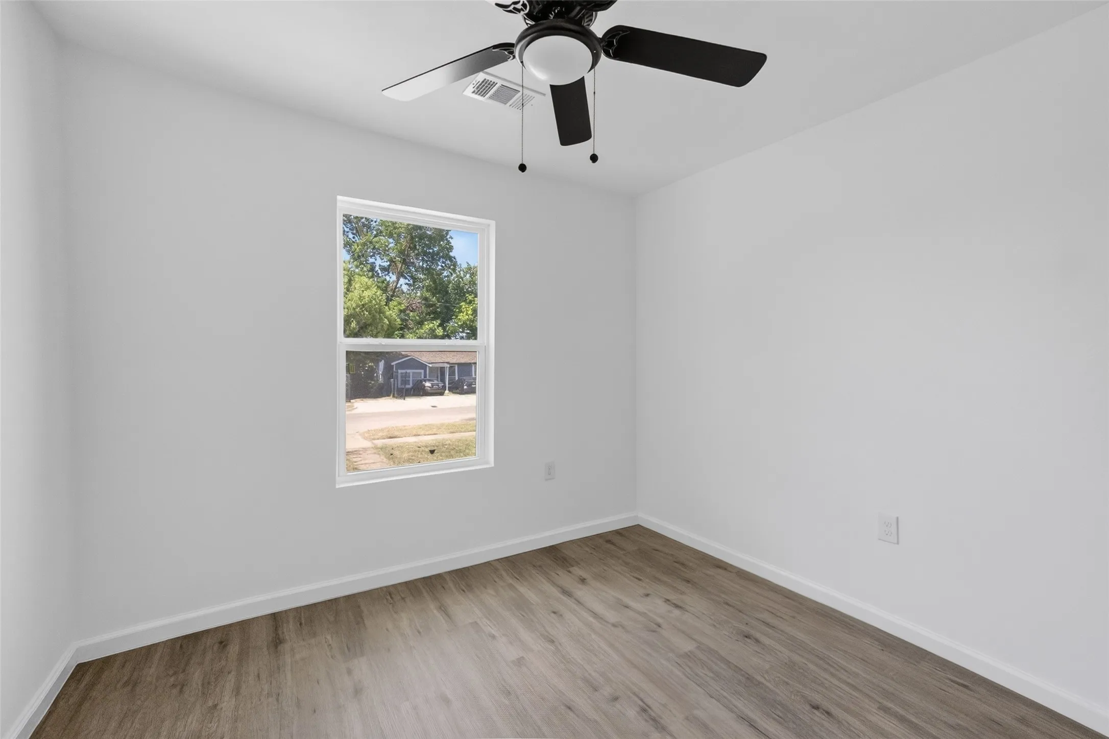 Room featuring wood-finish flooring, white baseboards, a white wall finish, a single window, and a black ceiling fan with an integrated light fixture