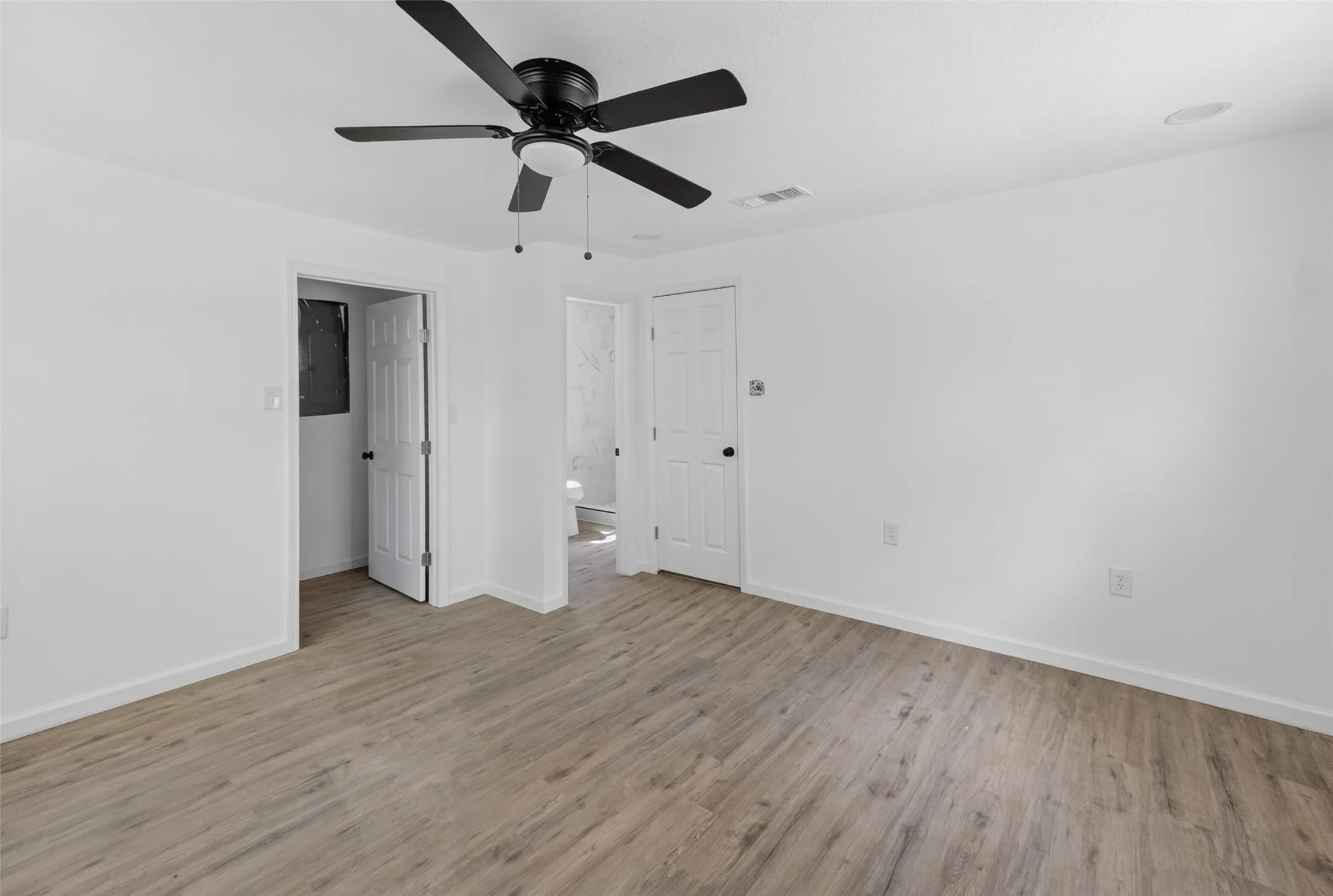 Expansive interior space featuring wood-finish flooring, crisp white walls, and a black ceiling fan with integrated lighting