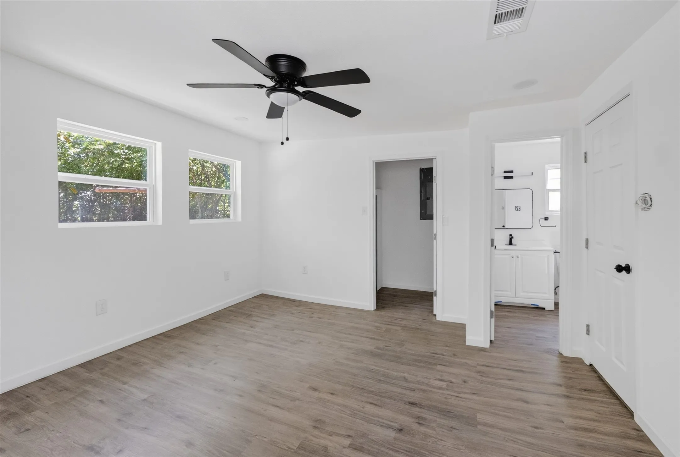 Open-concept room featuring wood-finish flooring, a ceiling fan, and two windows