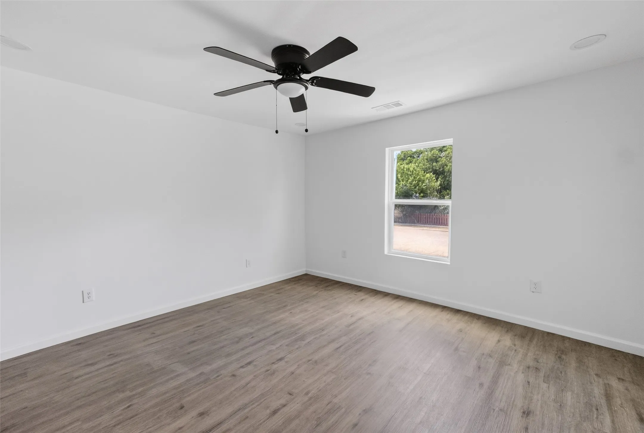 Spacious room featuring wood-finish flooring, white walls, and a black ceiling fan with integrated lighting