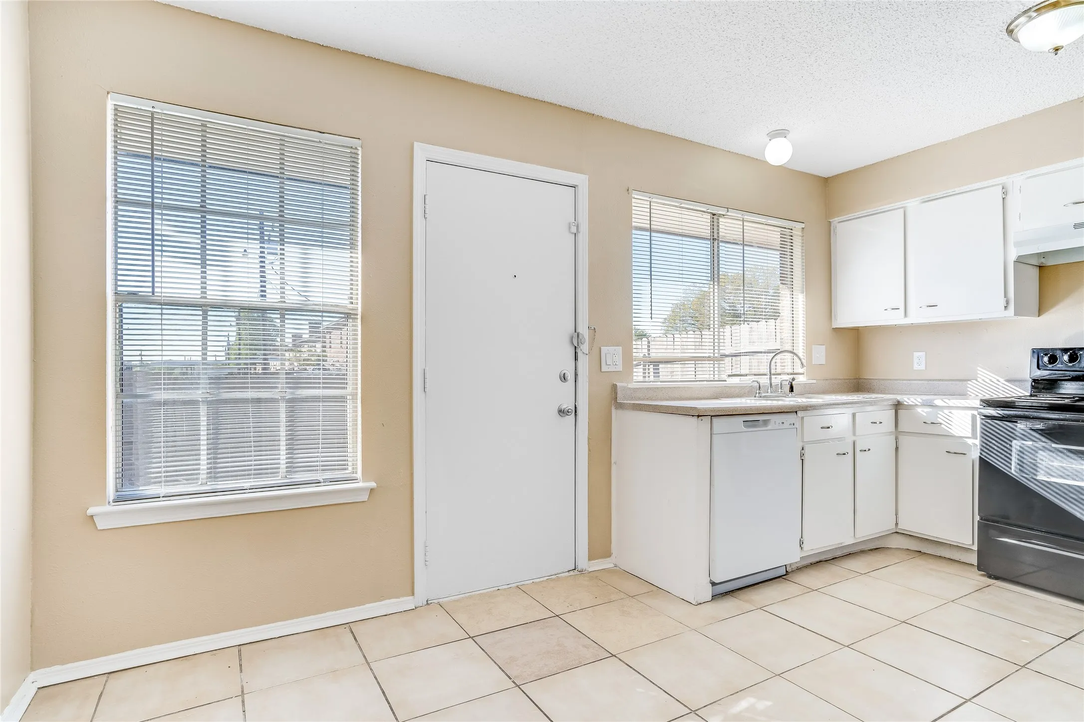 Kitchen with black electric range, dishwasher, white cabinetry, and light tile floors