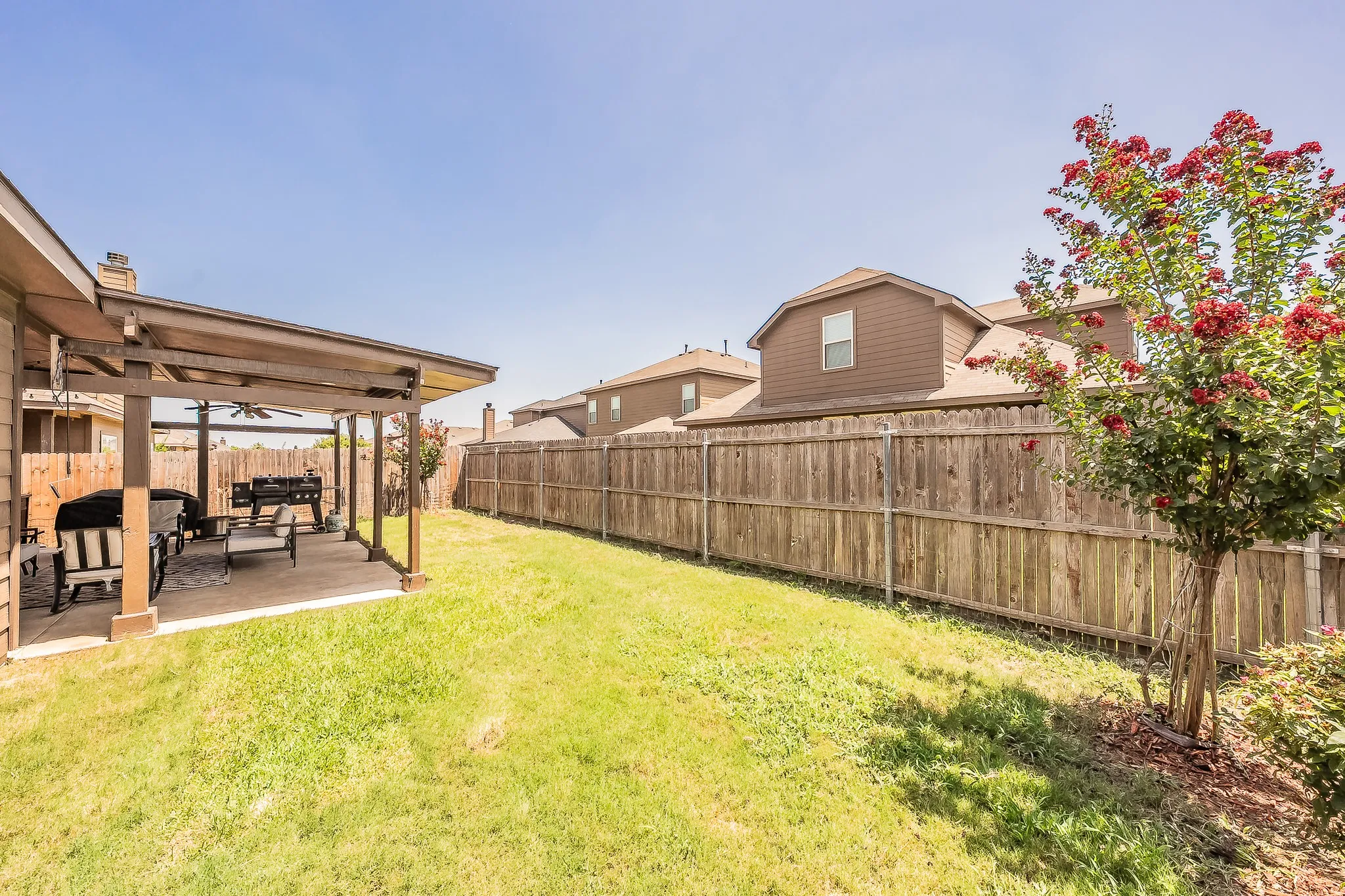 Expansive backyard featuring a covered patio with a ceiling fan, and a full wood privacy fence