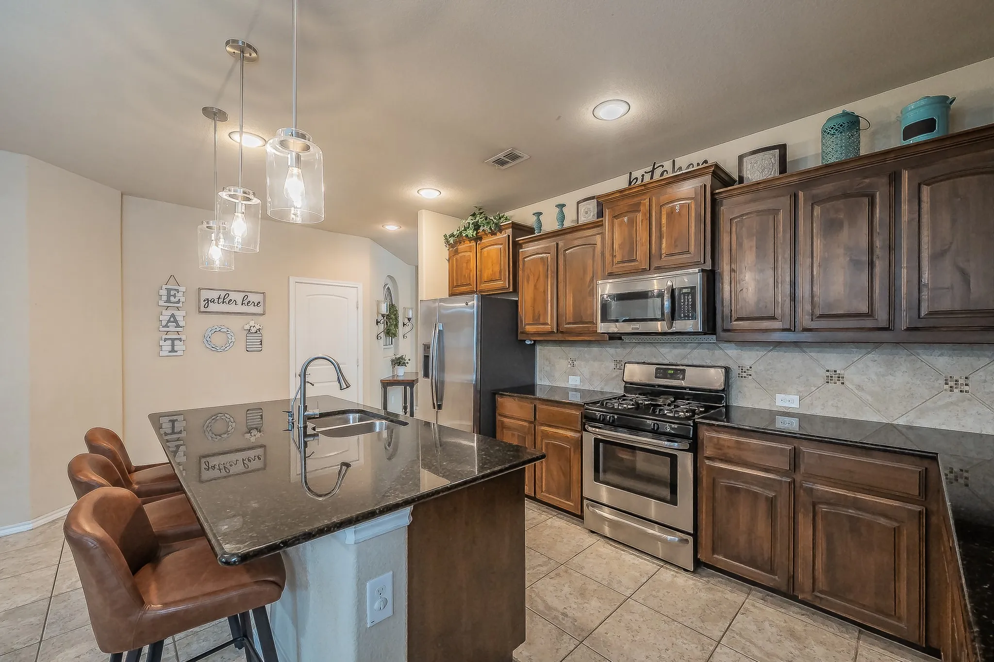 Kitchen featuring an island with a built-in sink, granite countertops, abundant cabinetry, and pendant lighting