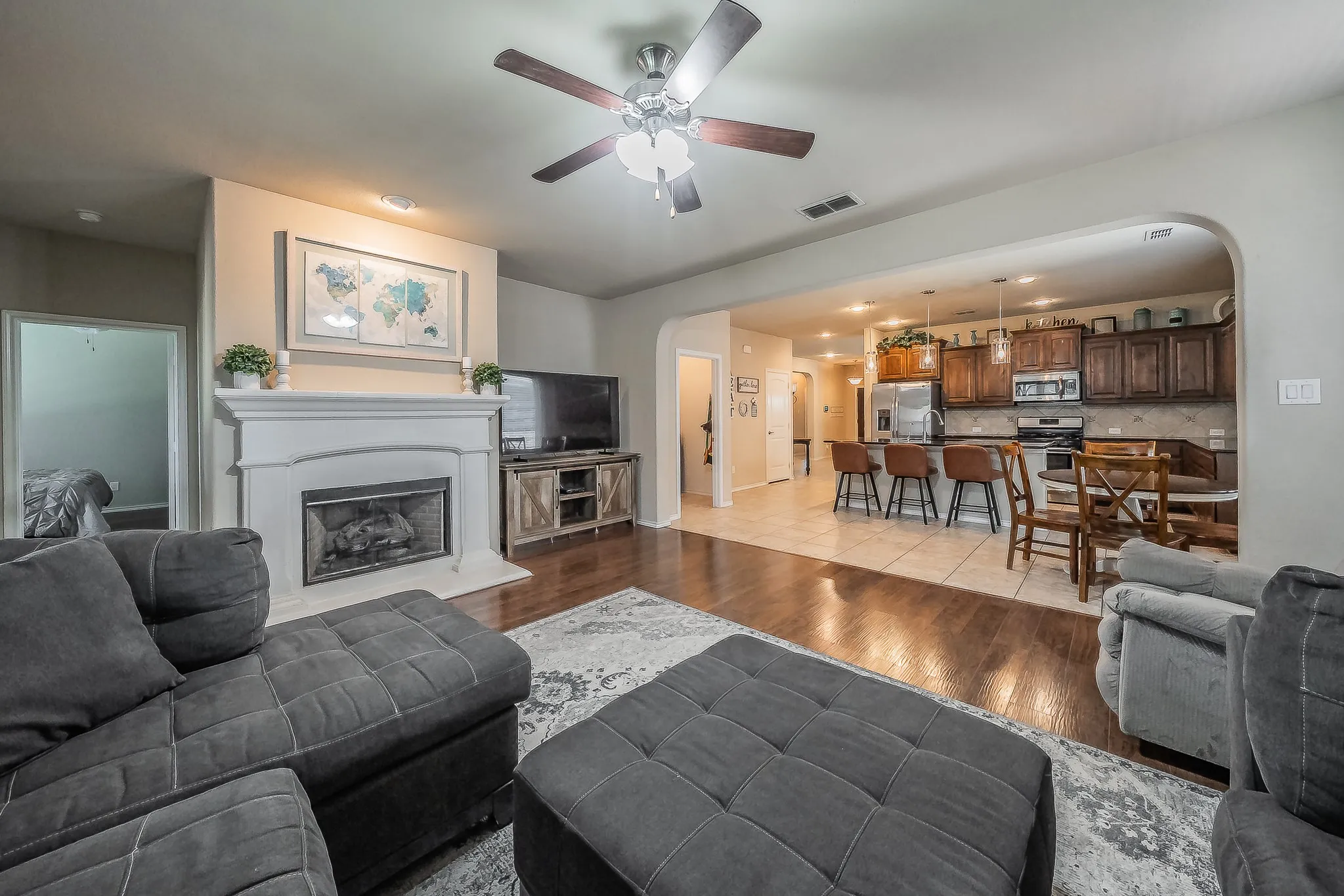 Spacious living area featuring a fireplace with white mantel, wood-finish flooring, and a ceiling fan