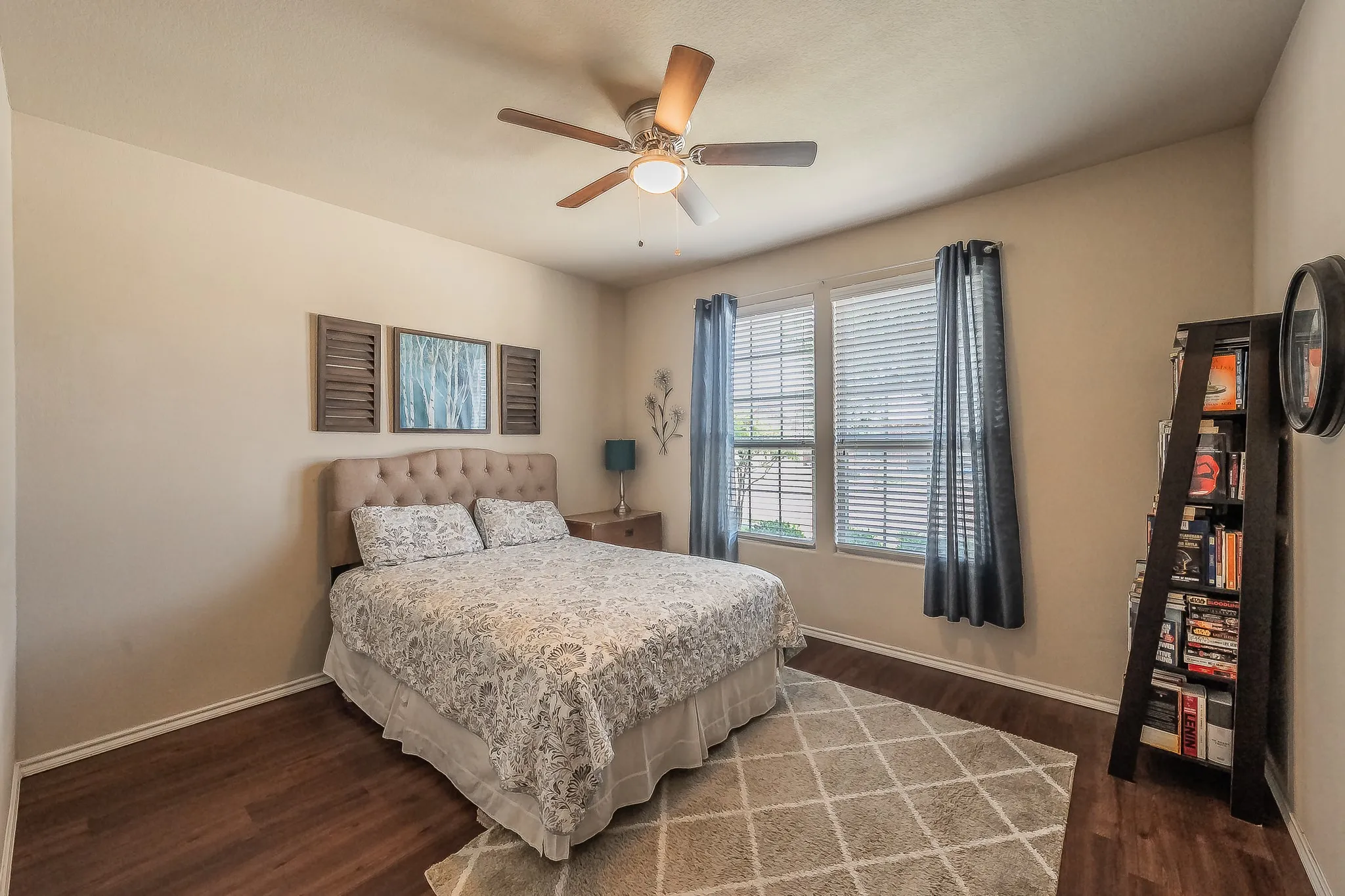 Bedroom featuring wood-finish luxury vinyl flooring, two large windows with blinds, a ceiling fan with integrated lighting, and neutral wall tones